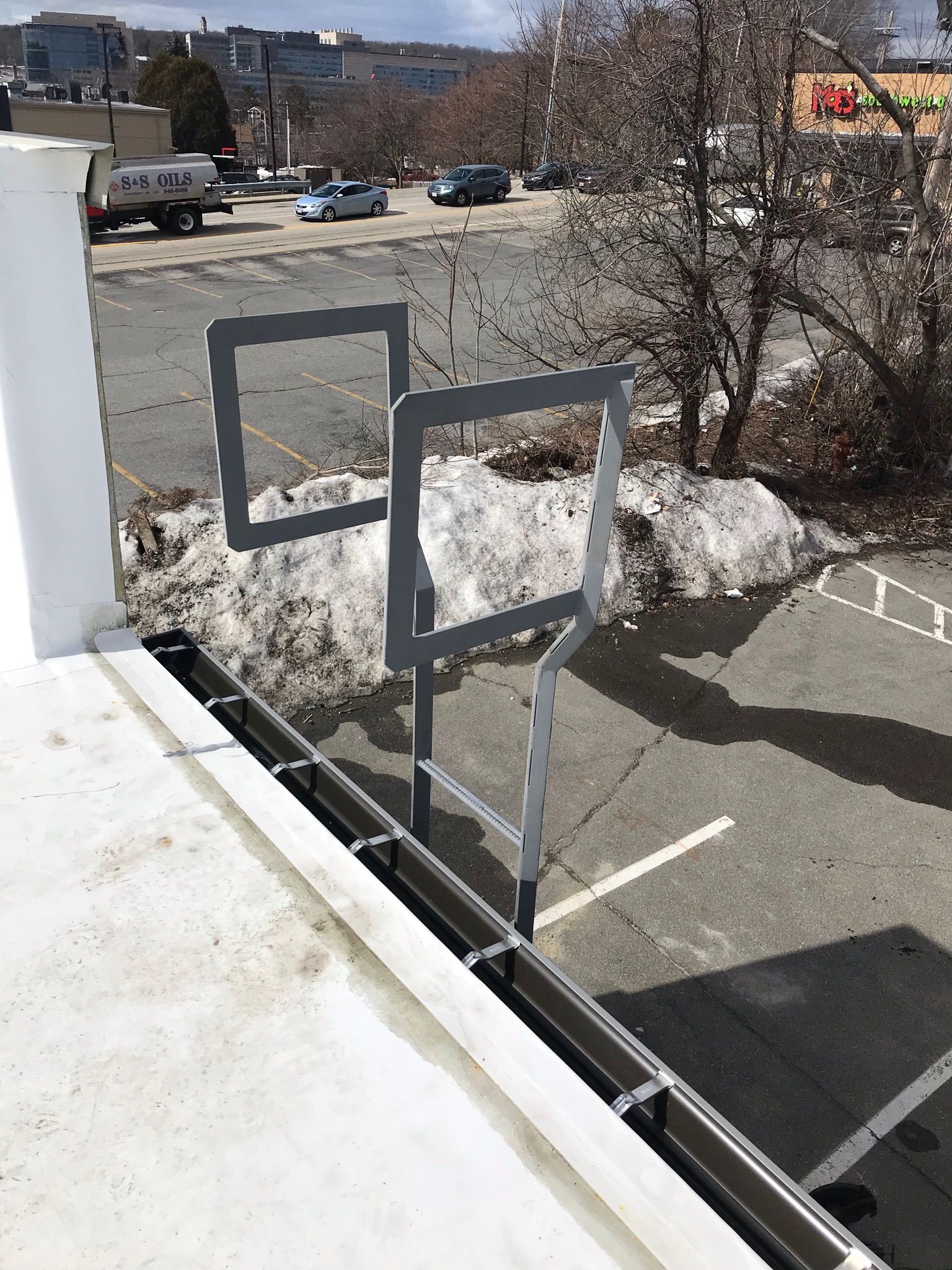 Parking lot view through a balcony railing with snowbanks, bare trees, and parked cars in the distance