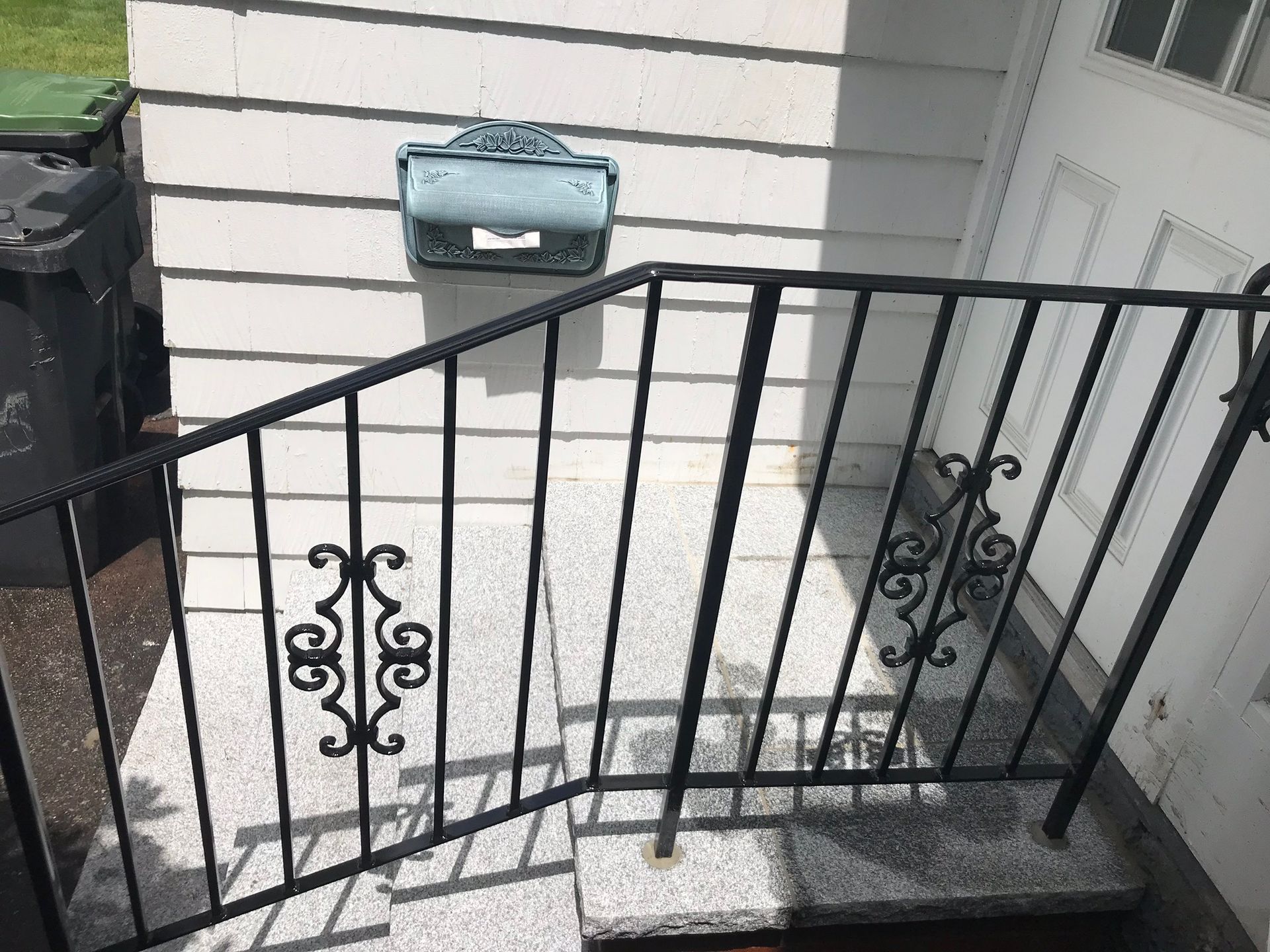 Front steps with black metal railing beside a house, leading to a door and wall-mounted mailbox.