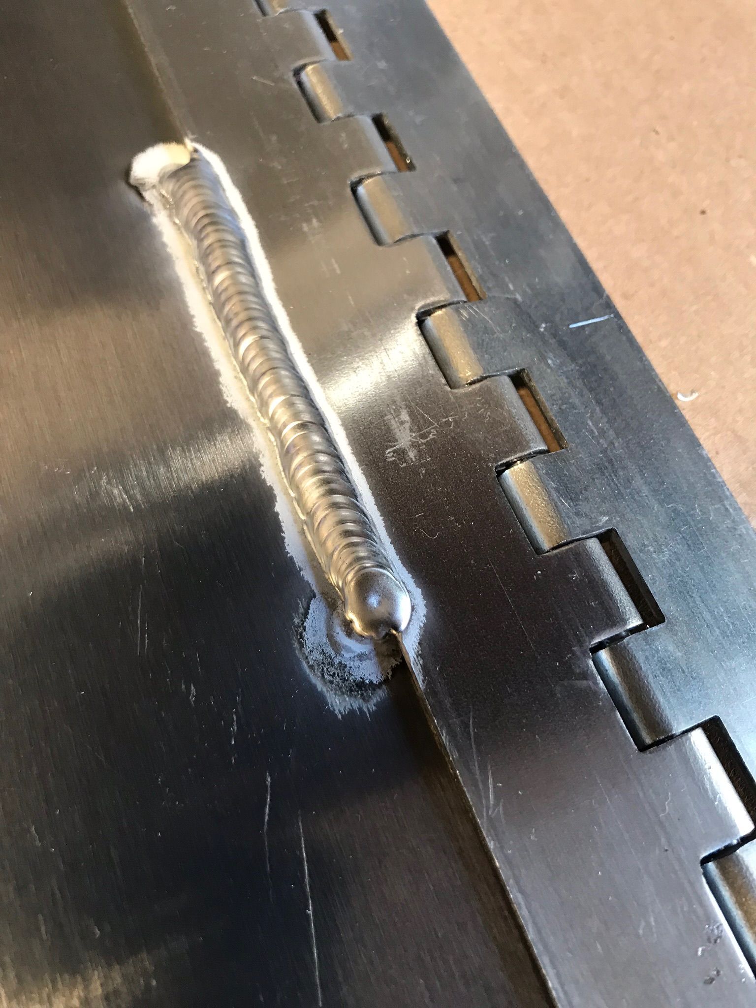Close-up of a shiny silver welded seam on a dark metal surface with interlocking edges nearby