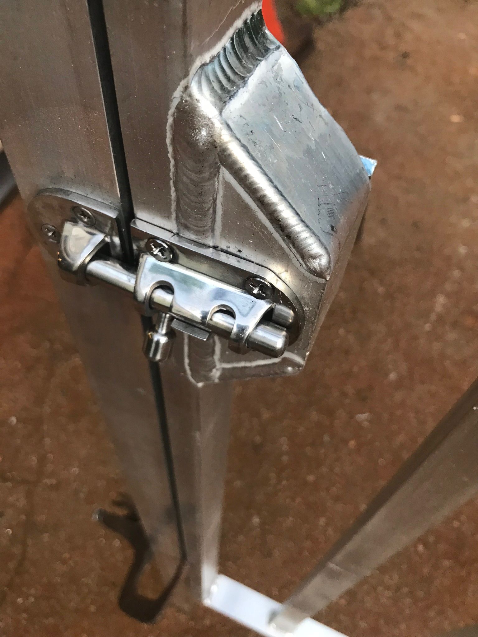 Close-up of a metal latch and cable on a glass door with a dark brown frame