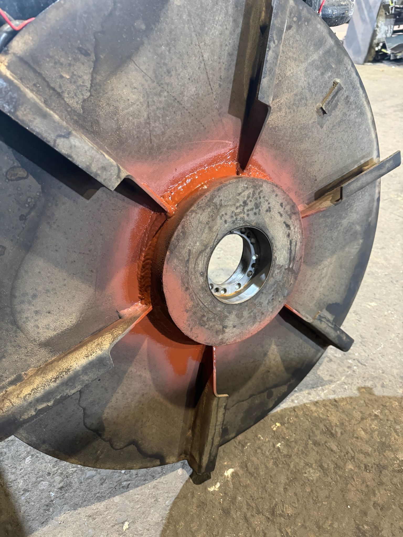 Close-up of a worn metal turbine impeller with rust and a central hub on a concrete surface