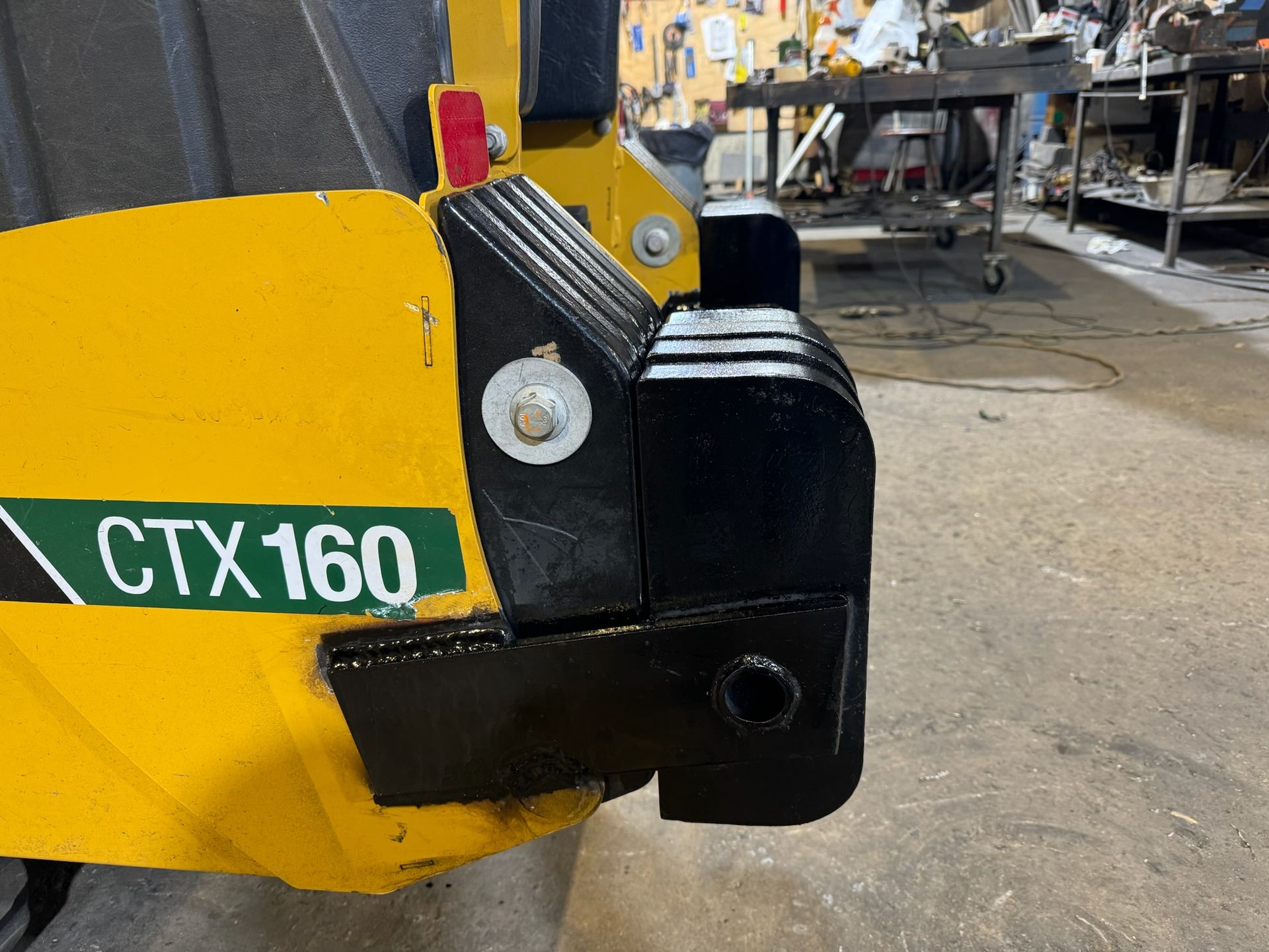 Close-up of a yellow CTX160 machine attachment in a workshop, showing a black metal coupling.