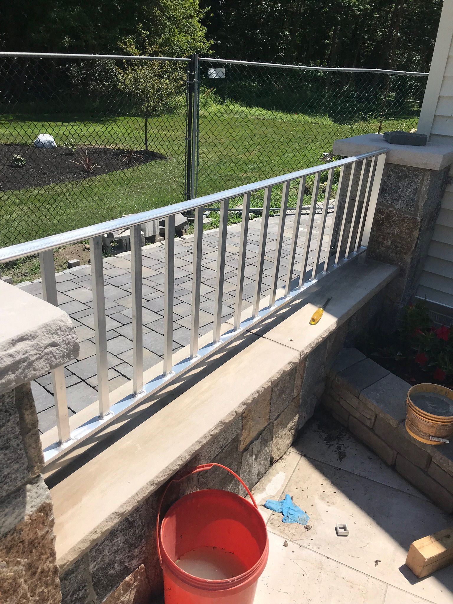 Outdoor patio with white railing, red bucket, and potted plants in bright sunlight