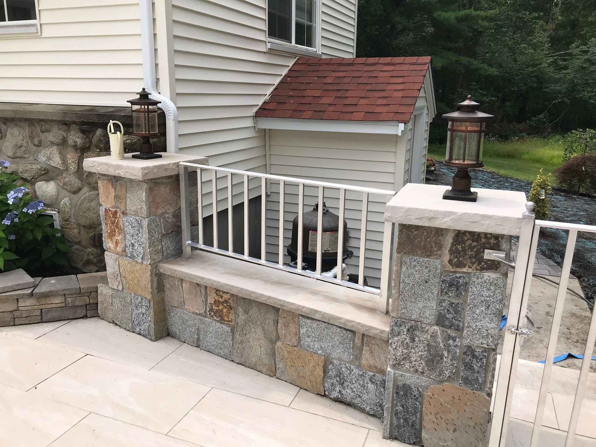 Stone-and-white railing beside a house, with lanterns on the posts and a small shed in the background.