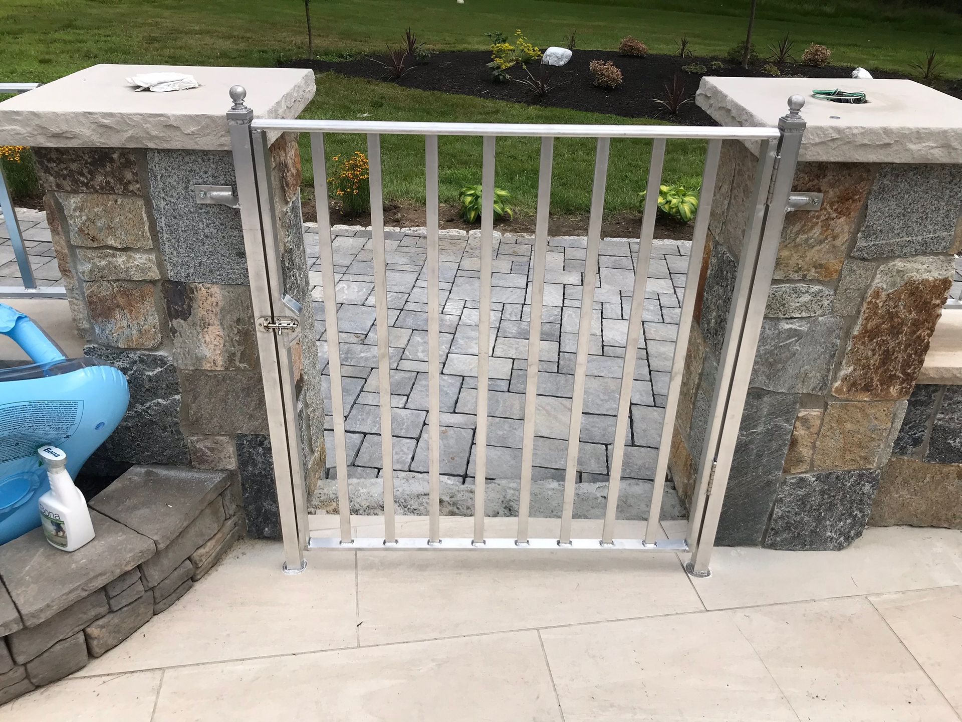 White metal gate between stone pillars at the top of a paved driveway.