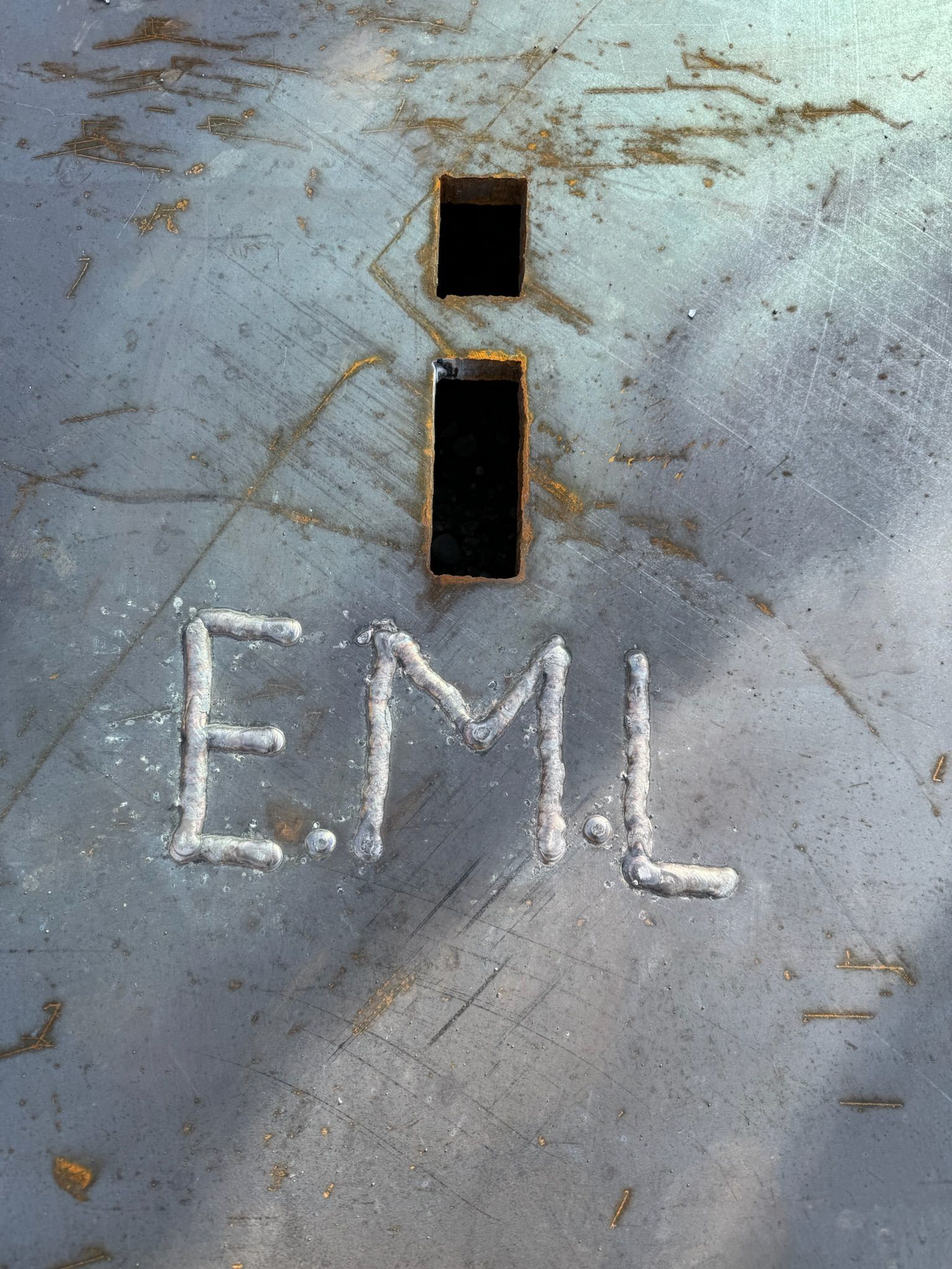 Blue-gray metal surface with a keyhole slot and white chalk letters “EML” below it.