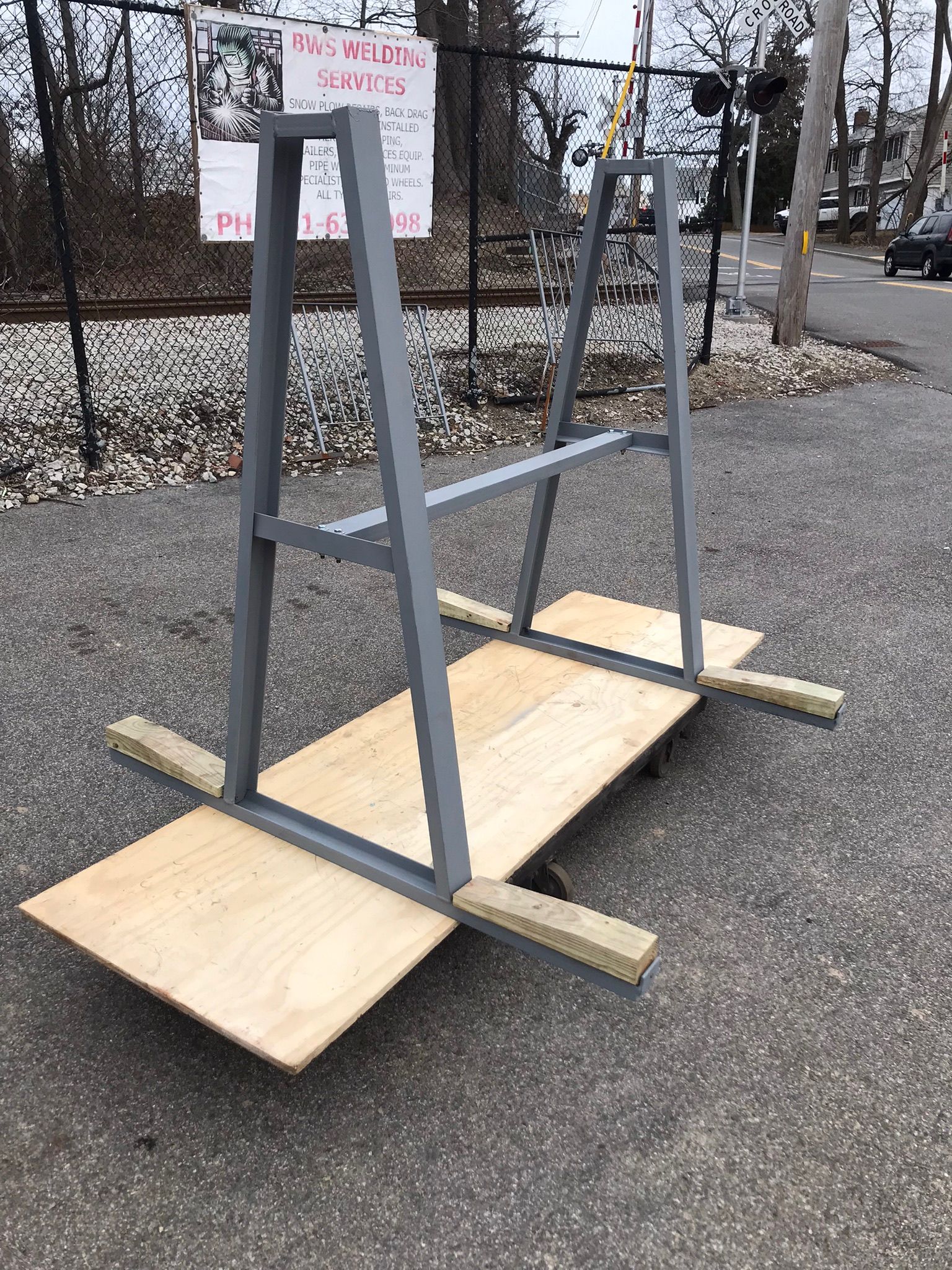 Gray metal A-frame structure on a wooden sled base outdoors on pavement, with a snowy background