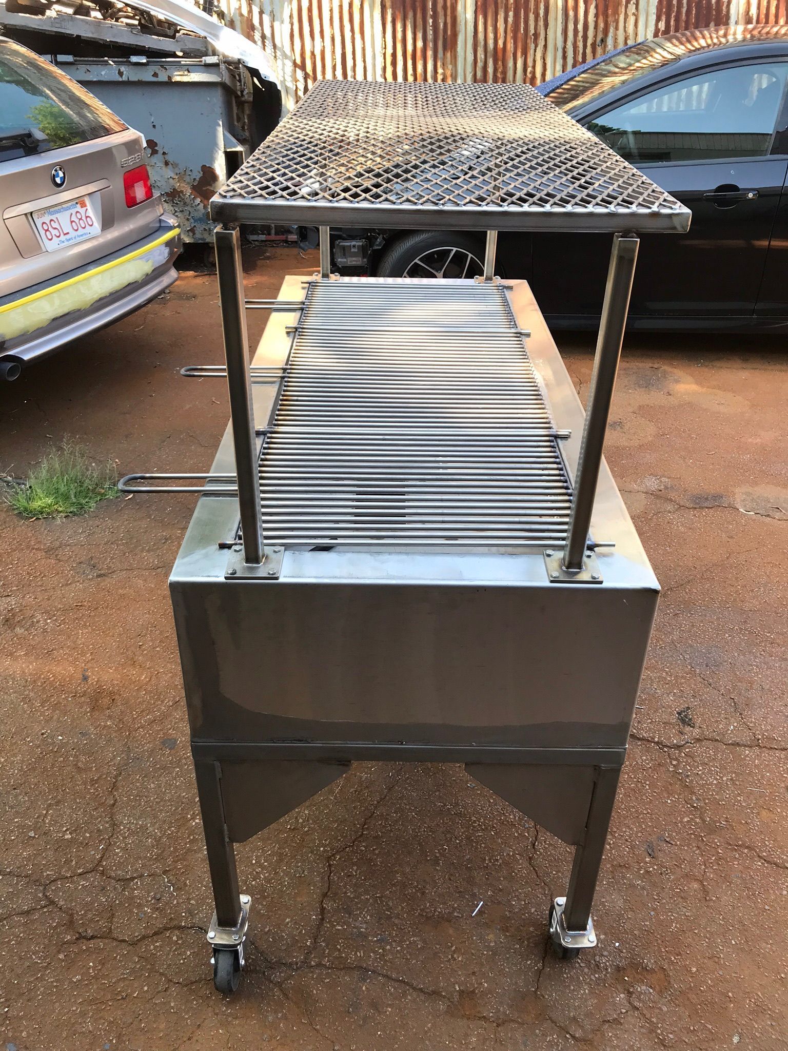 Metal conveyor machine with slatted top and wheeled base on a dirt surface outdoors