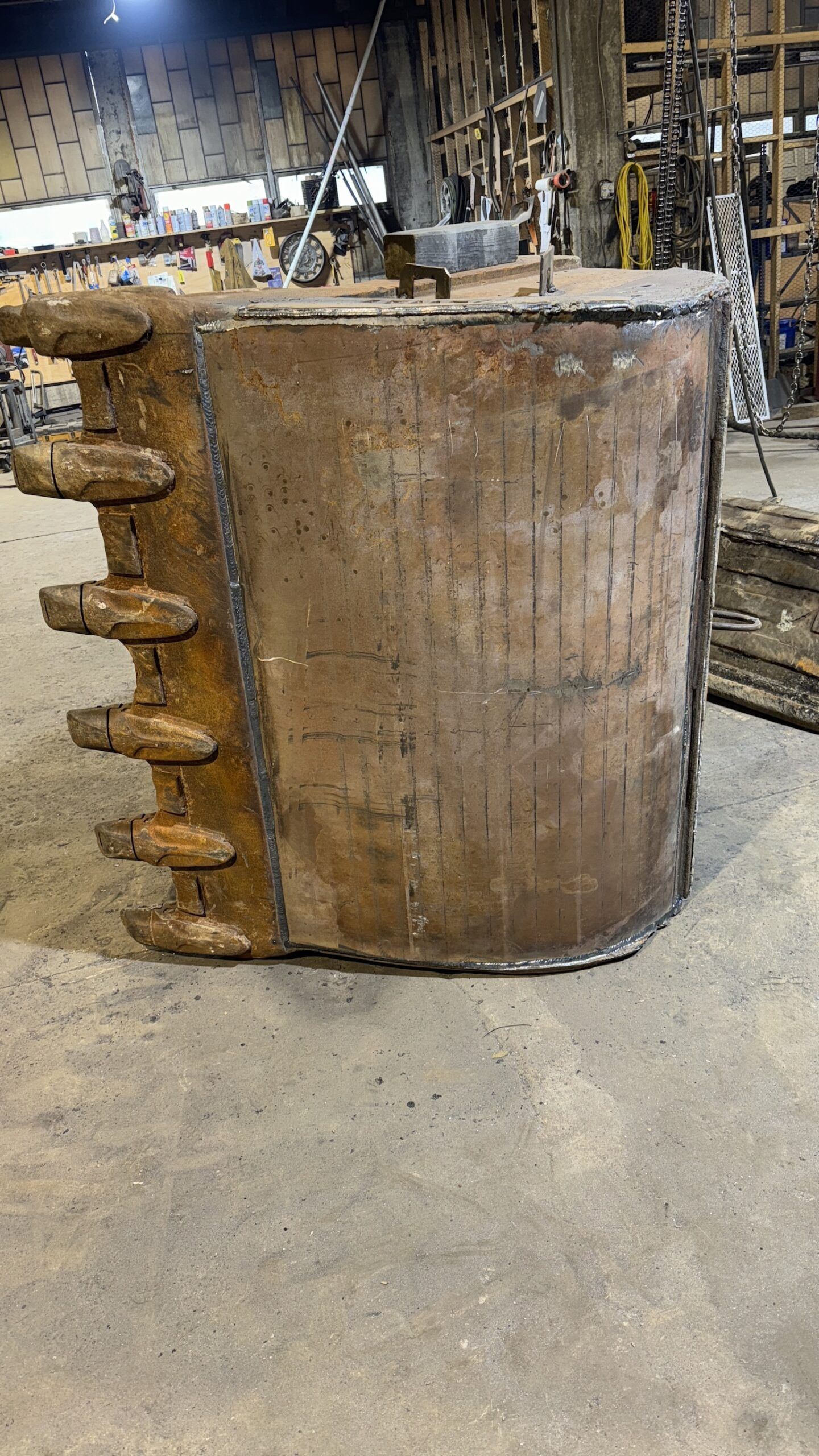 Large rusted industrial metal cylinder with protruding side lugs in a workshop setting
