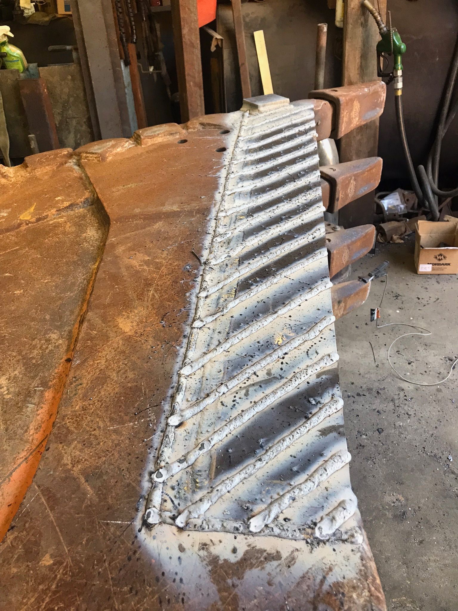 Metal corrugated sheet with diagonal ridges leaning against a workshop surface, covered in white residue