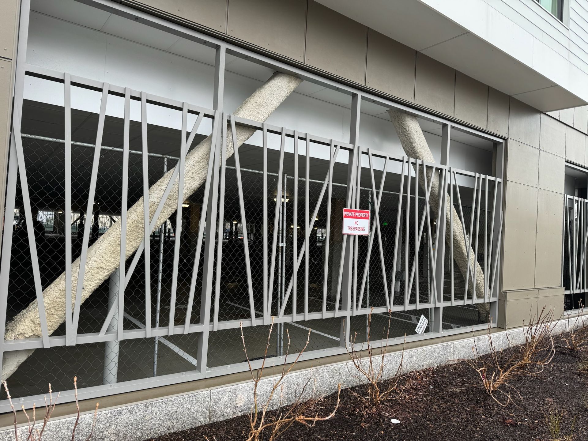 Bent metal security bars blocking a building window, with a warning sign and broken glass behind them