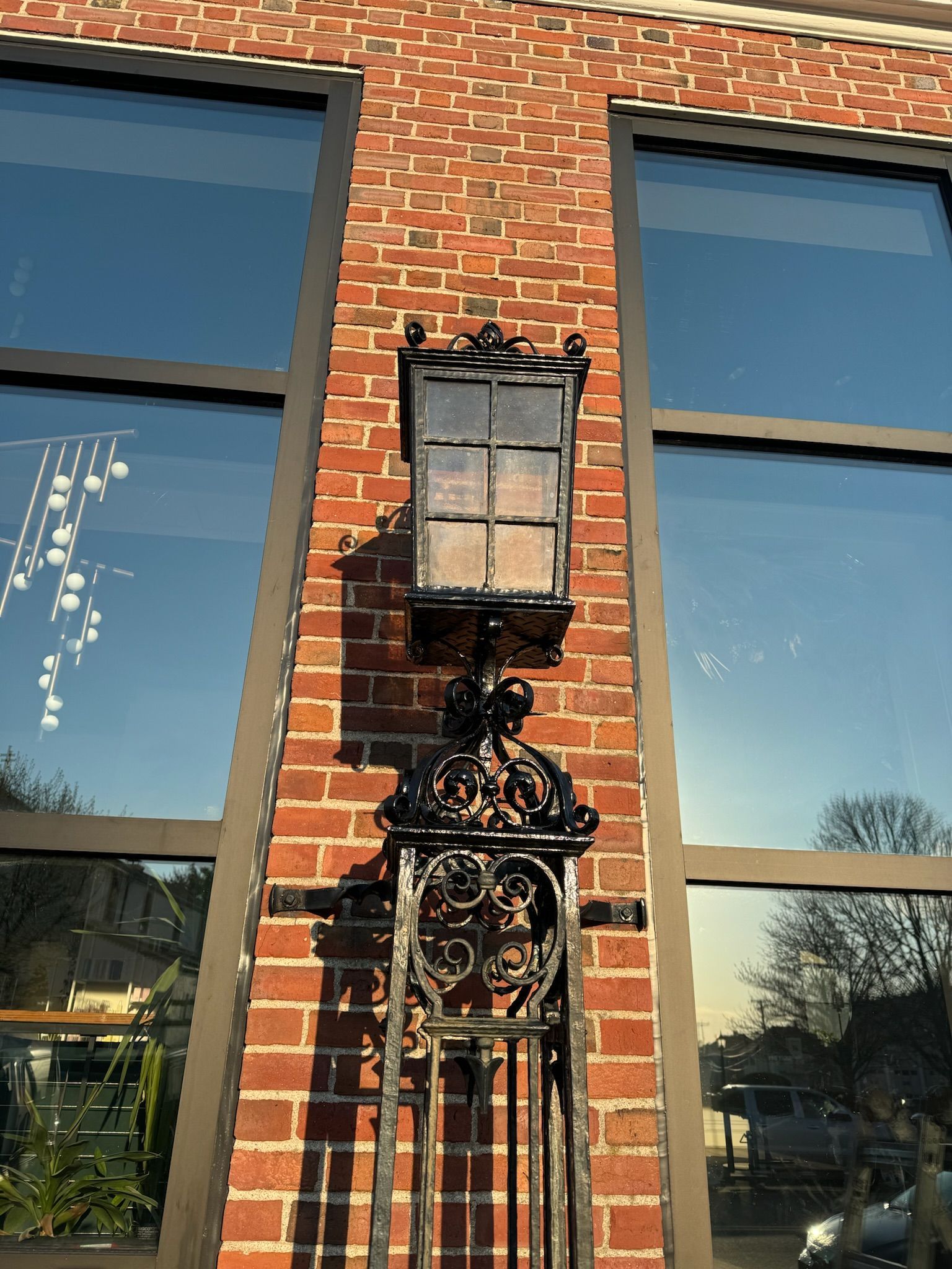 Ornate black metal wall lantern on a red brick building between two windows