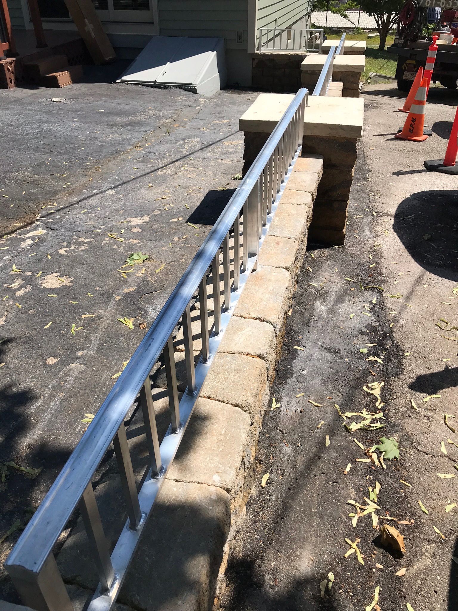 Blue handrail along a low stone wall beside a cracked sidewalk and construction cones on a street