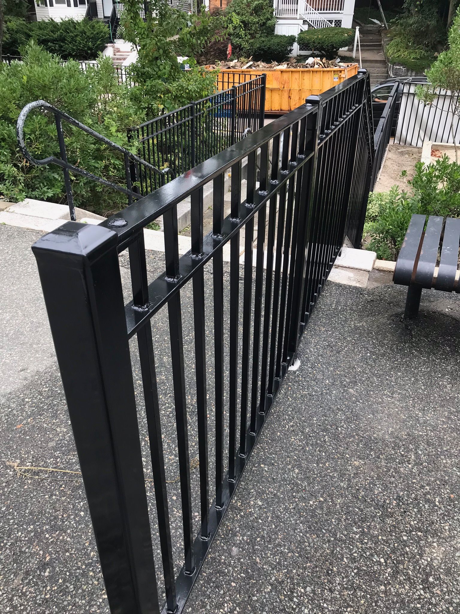 Black metal railing beside a gravel path with outdoor seating in a garden area