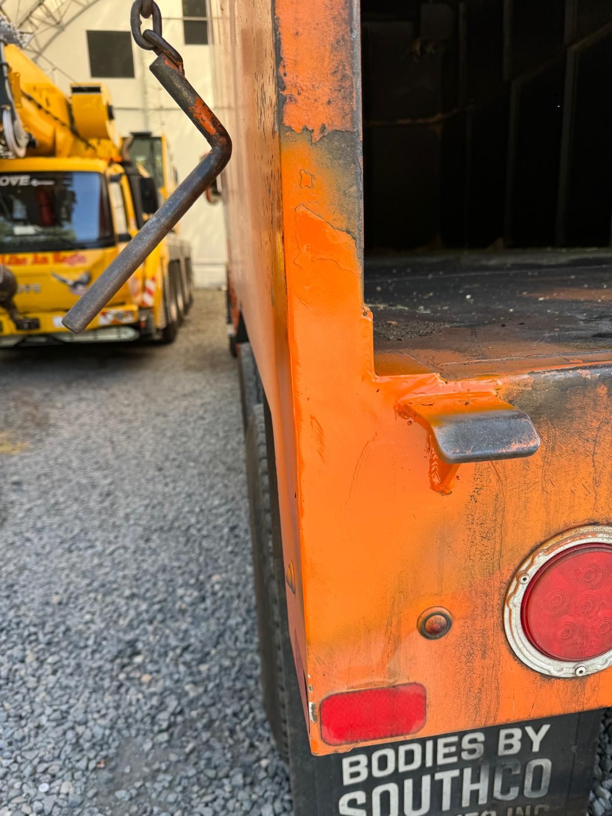 Orange truck bed with “BODIES BY SOUTHCO” text, beside a yellow forklift on gravel.