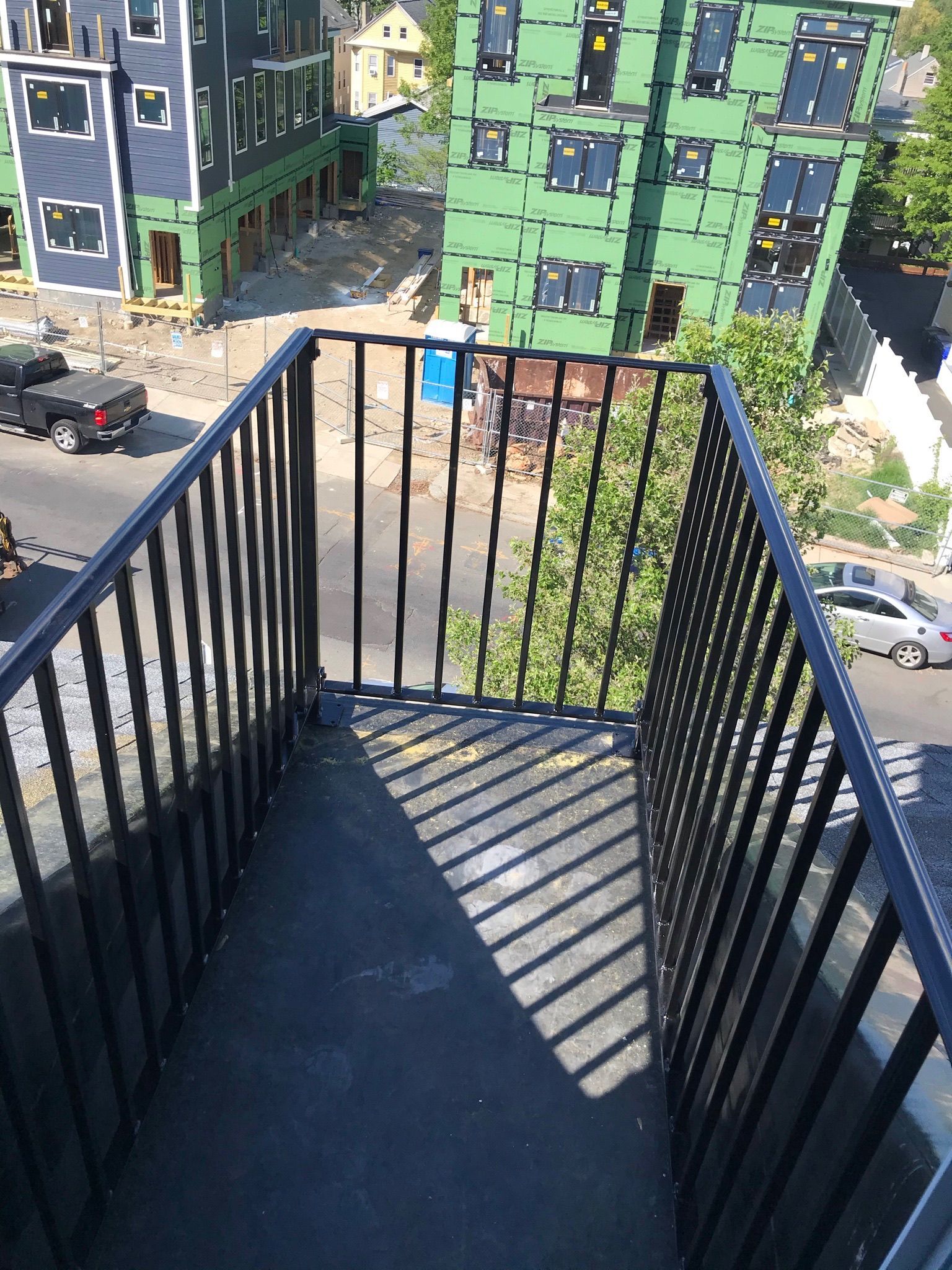Balcony railing overlooking a construction site with green buildings and parked cars below