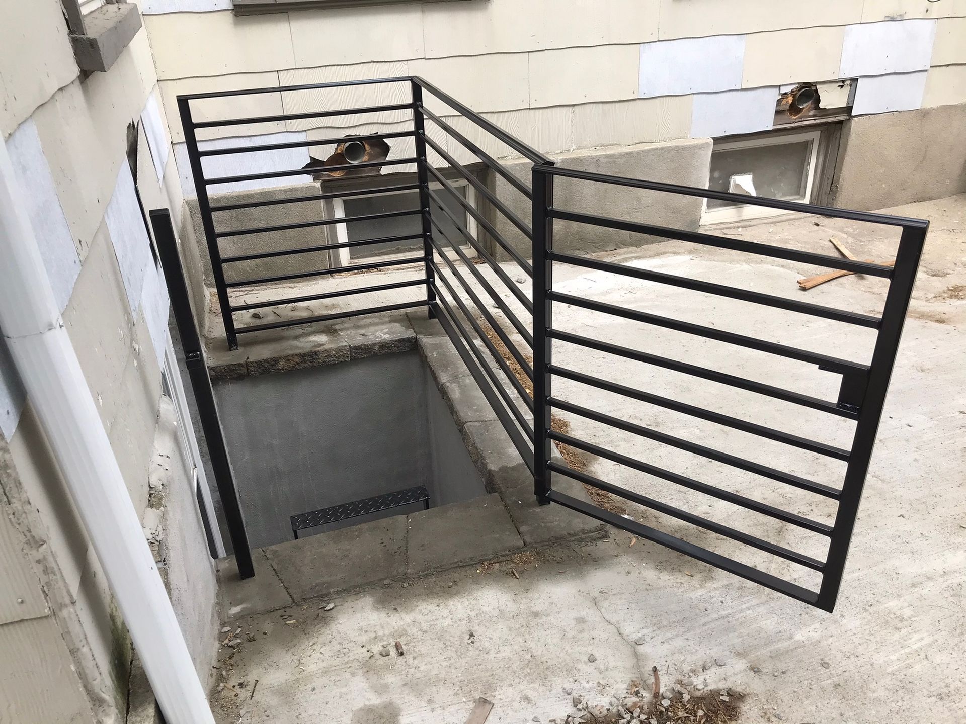 Black metal stair railing around a concrete stairwell with a person sitting on the landing.