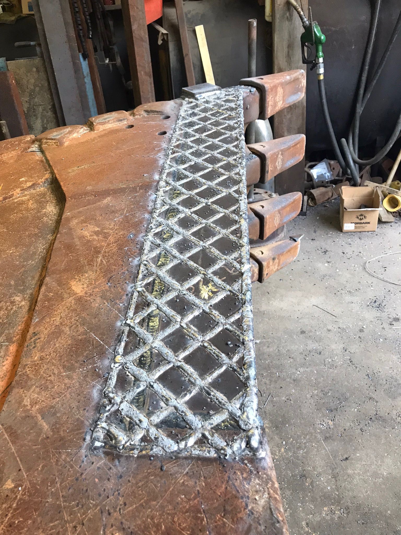 Metal diamond-pattern ramp panel on a workshop floor beside stacked lumber and tools