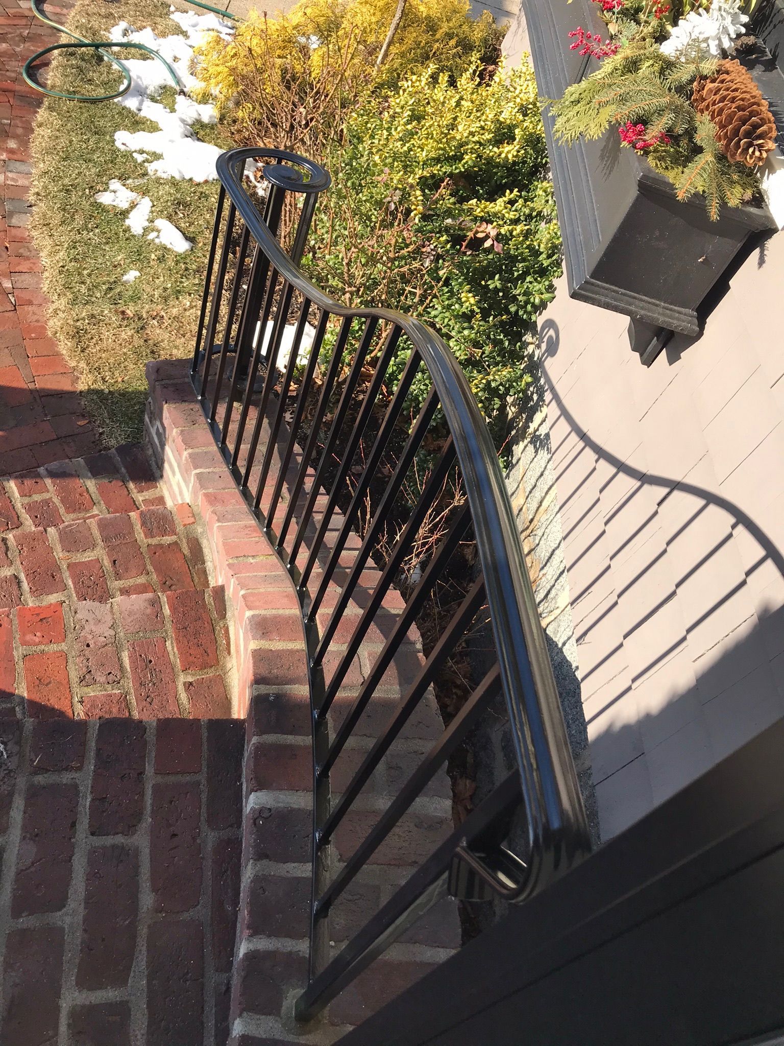 Black metal railing beside brick steps and a hanging flower basket in a sunlit garden path