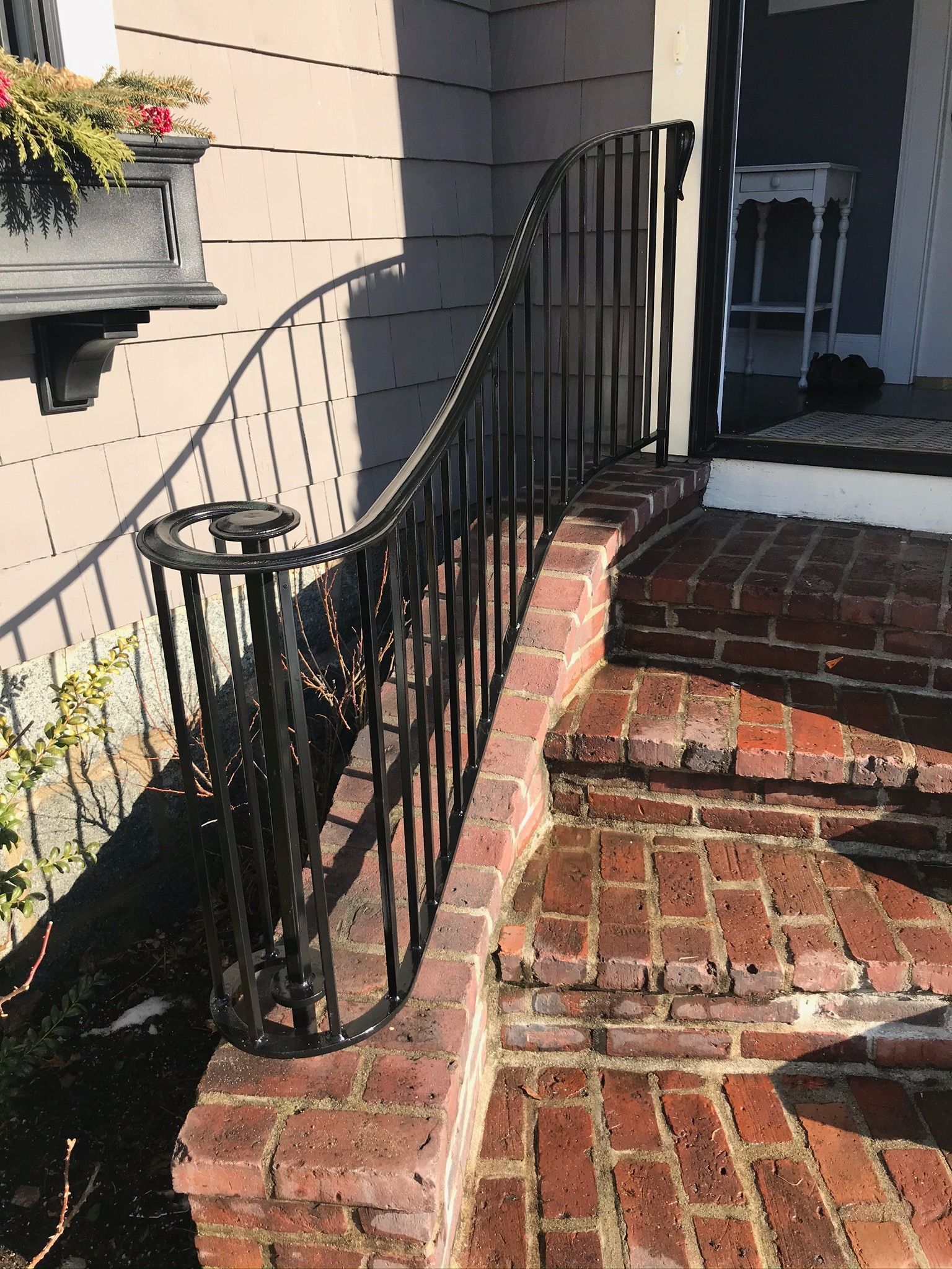Brick front steps with black wrought-iron railing leading to a house entrance.