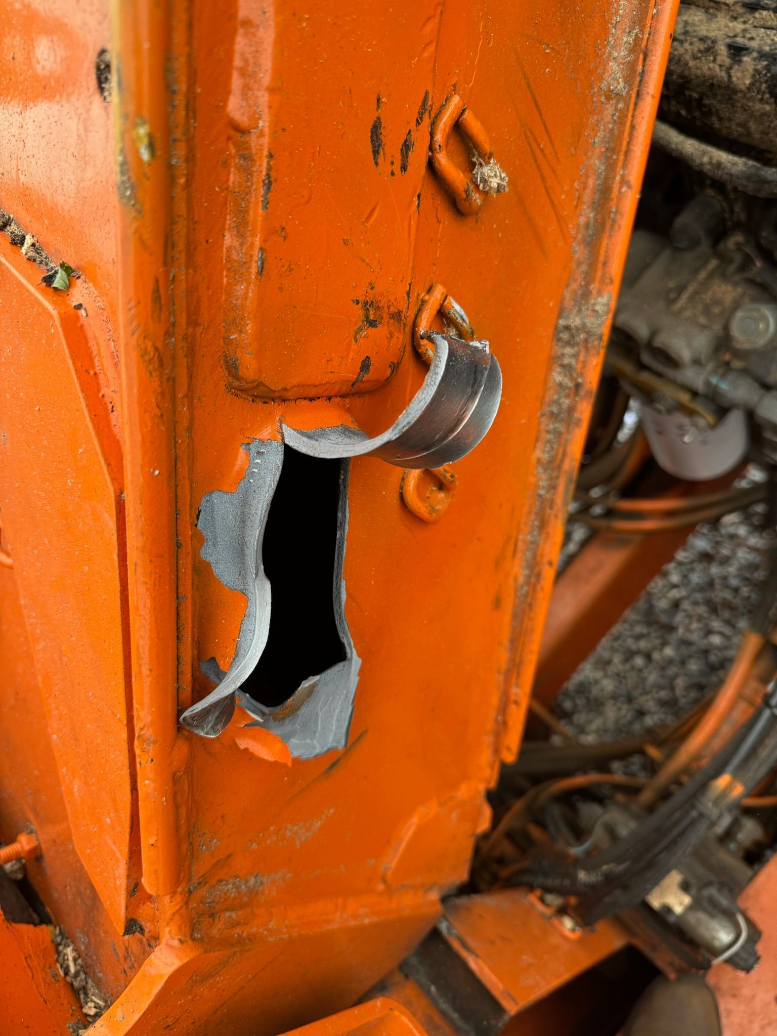 Close-up of a damaged orange metal panel with a large torn hole and visible wiring inside