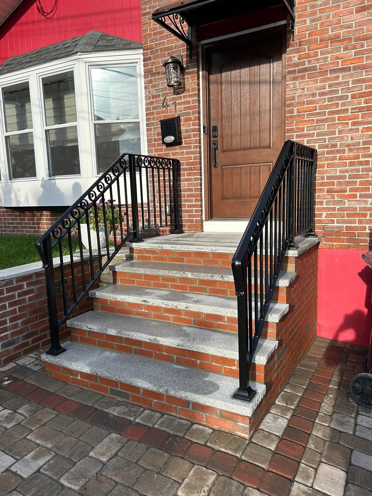 Brick house entrance with stairs, black railings, and a wooden front door