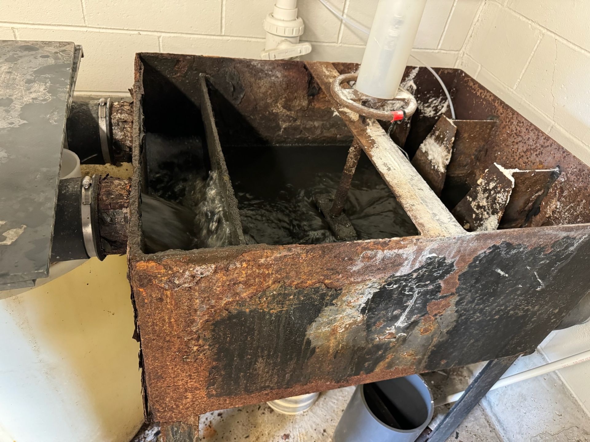 Rusty industrial water tank with pipes and flowing water inside a tiled utility room
