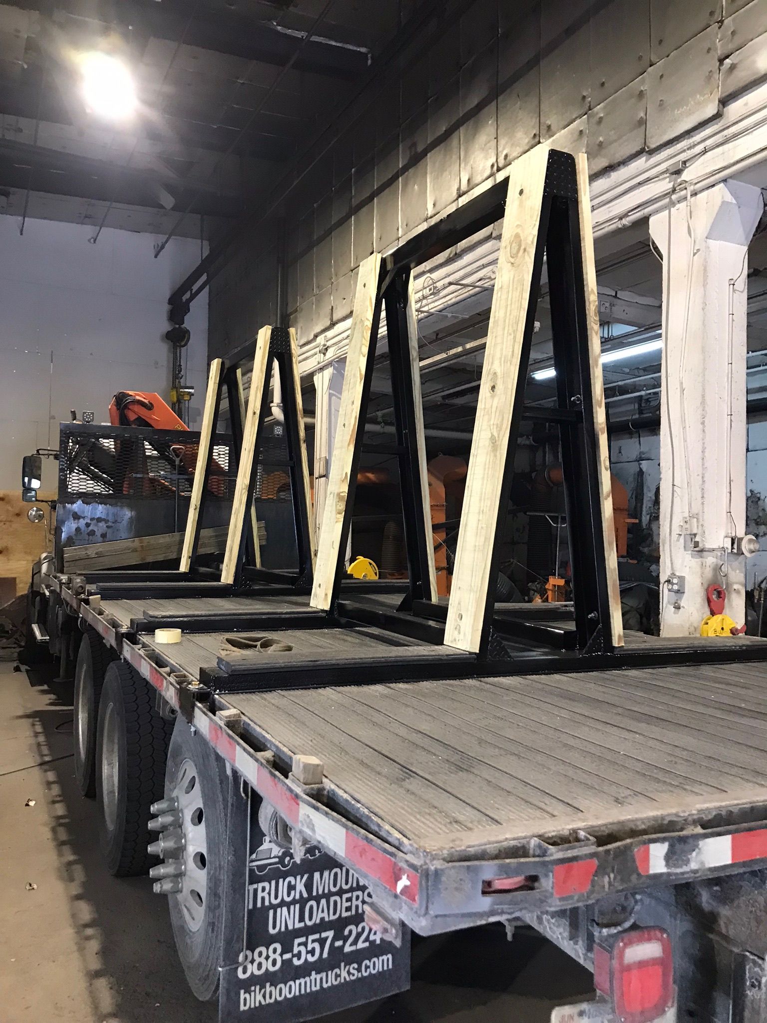 Flatbed truck inside a warehouse carrying several large wooden A-frame structures.