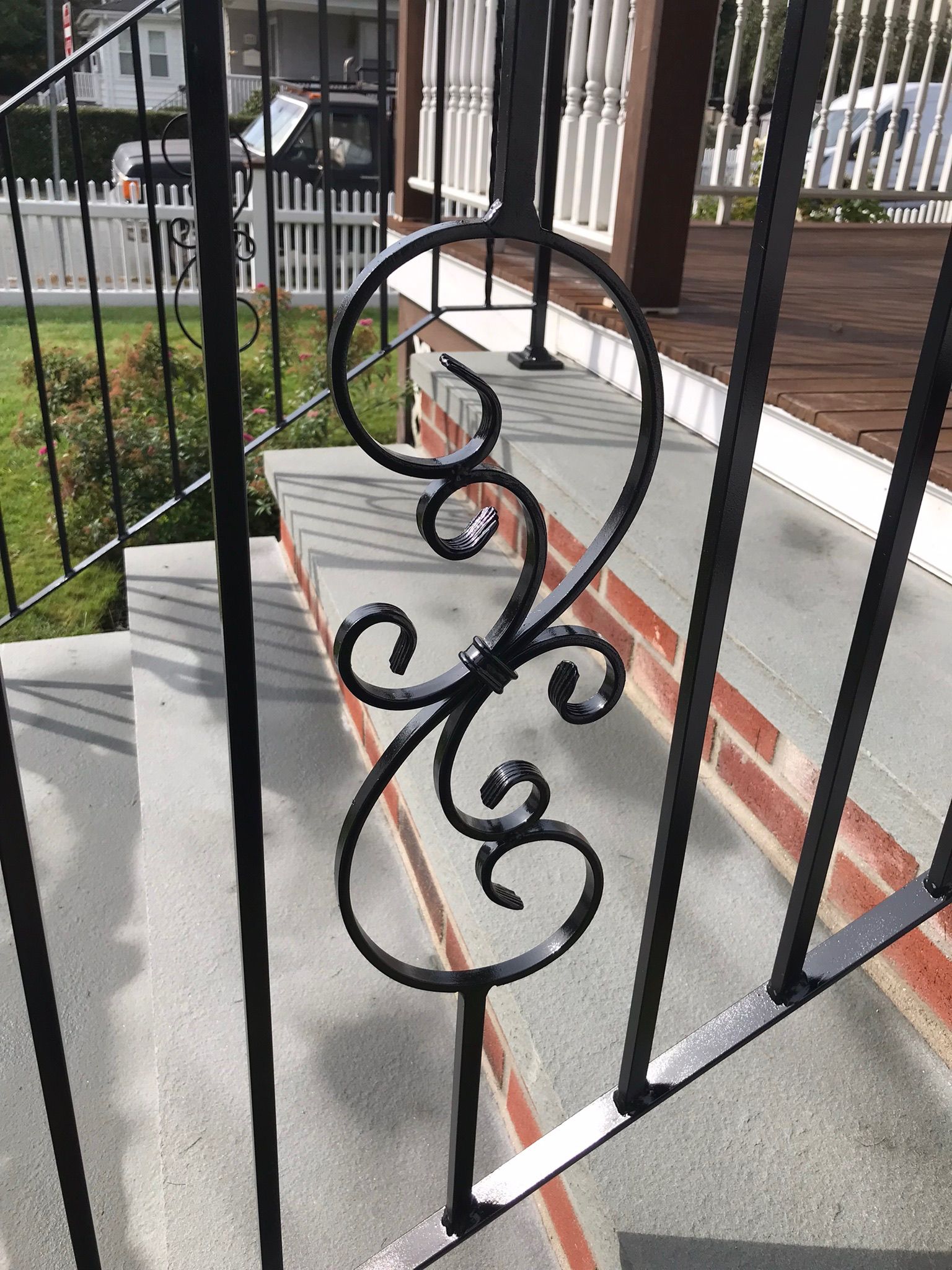 Black wrought-iron porch railing with decorative scrollwork and a circular top detail on a front porch
