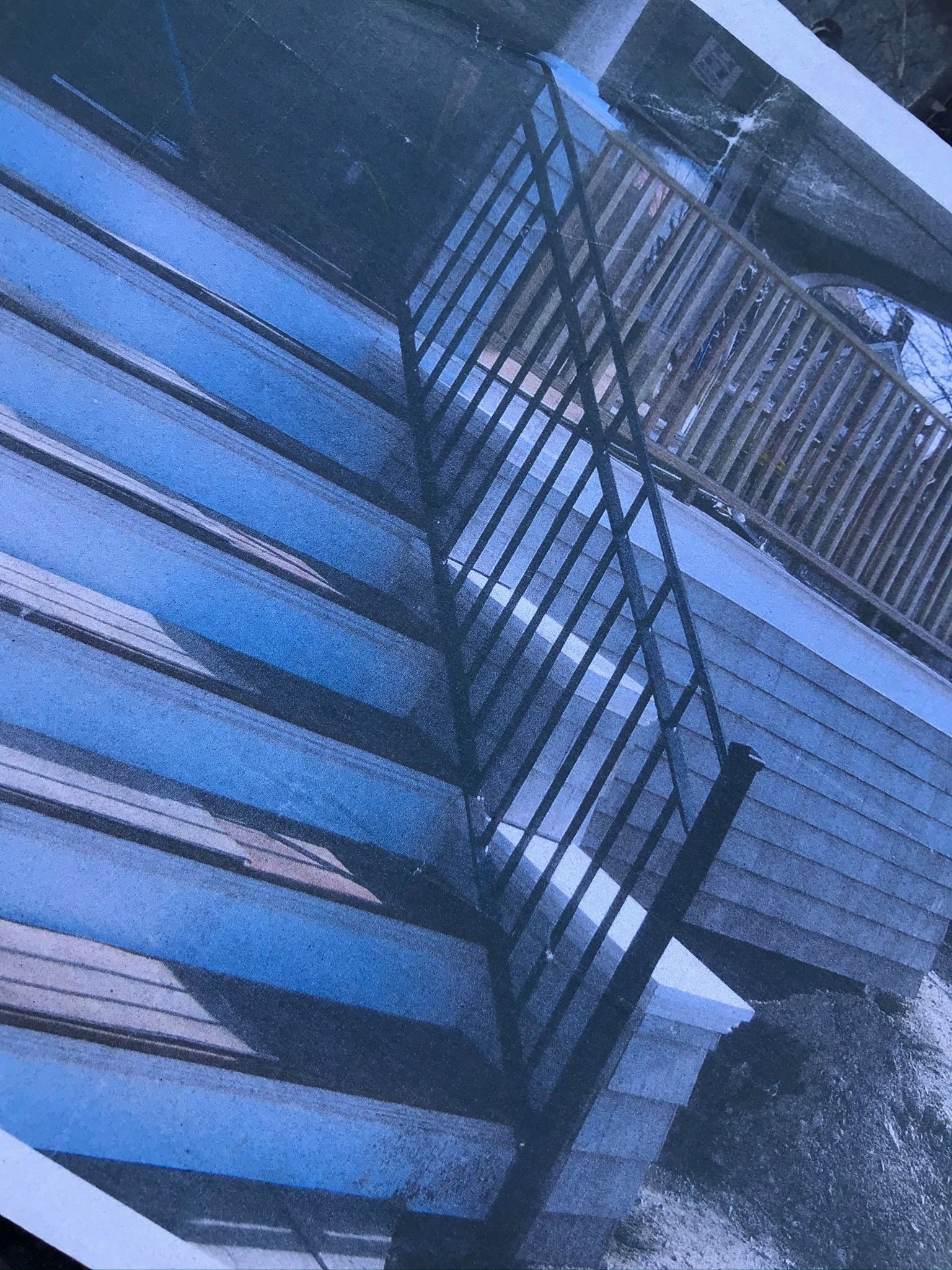 Blue-tinted close-up of a metal fire escape or staircase beside a building facade