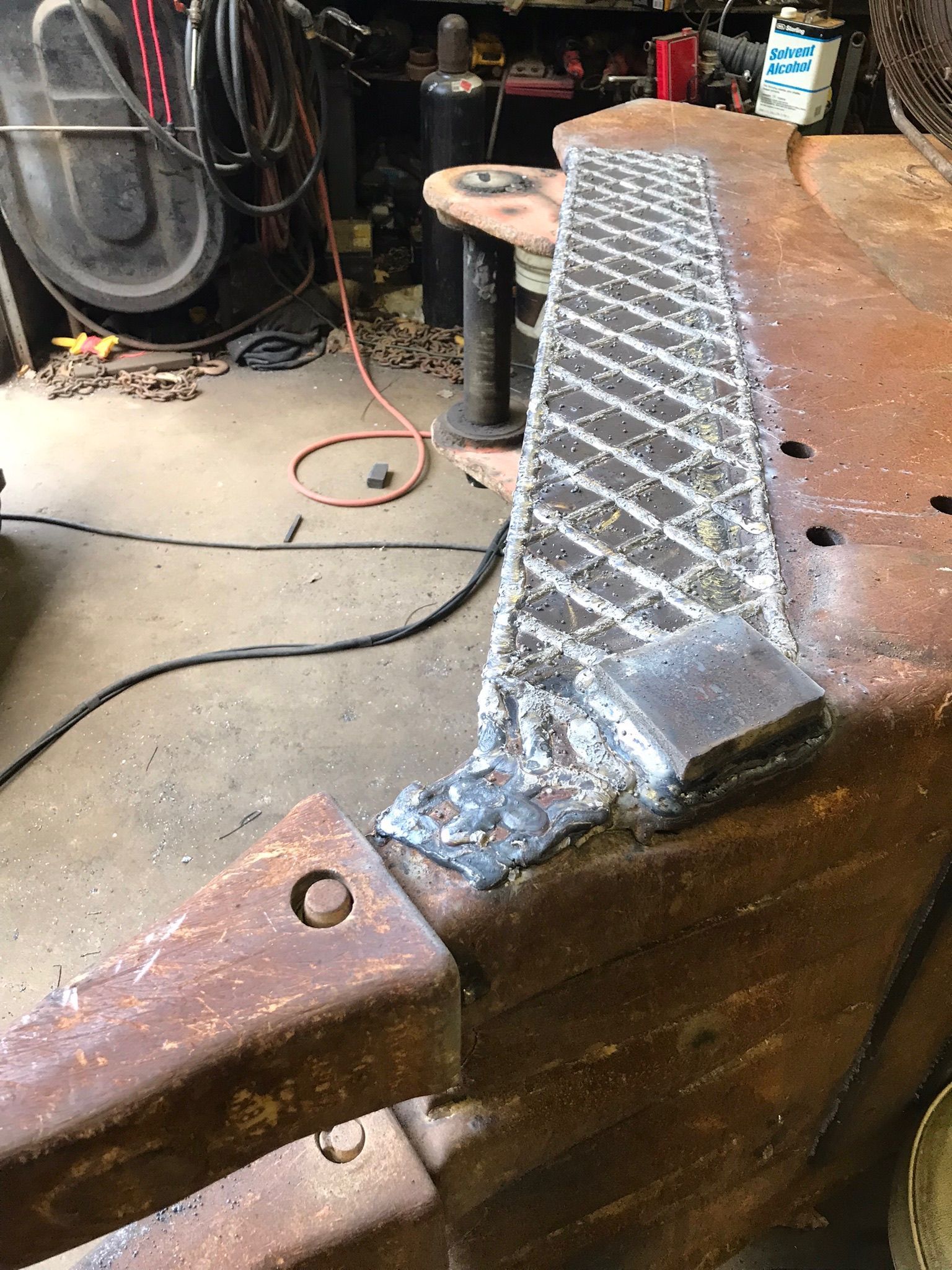 Close-up of a welded metal repair on a rusty brown part in a workshop.
