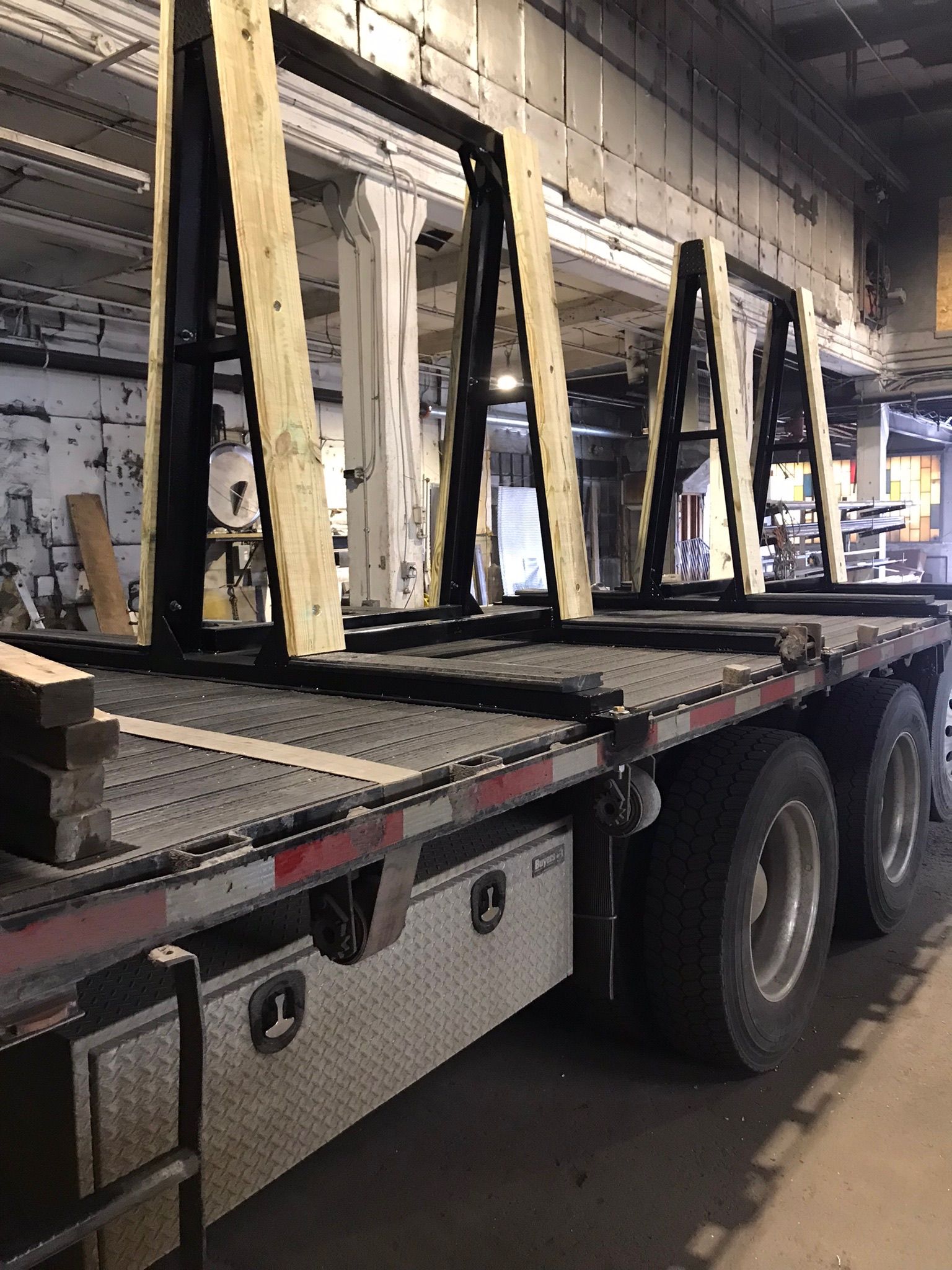 Flatbed truck carrying large wooden A-frame structures in an indoor industrial space