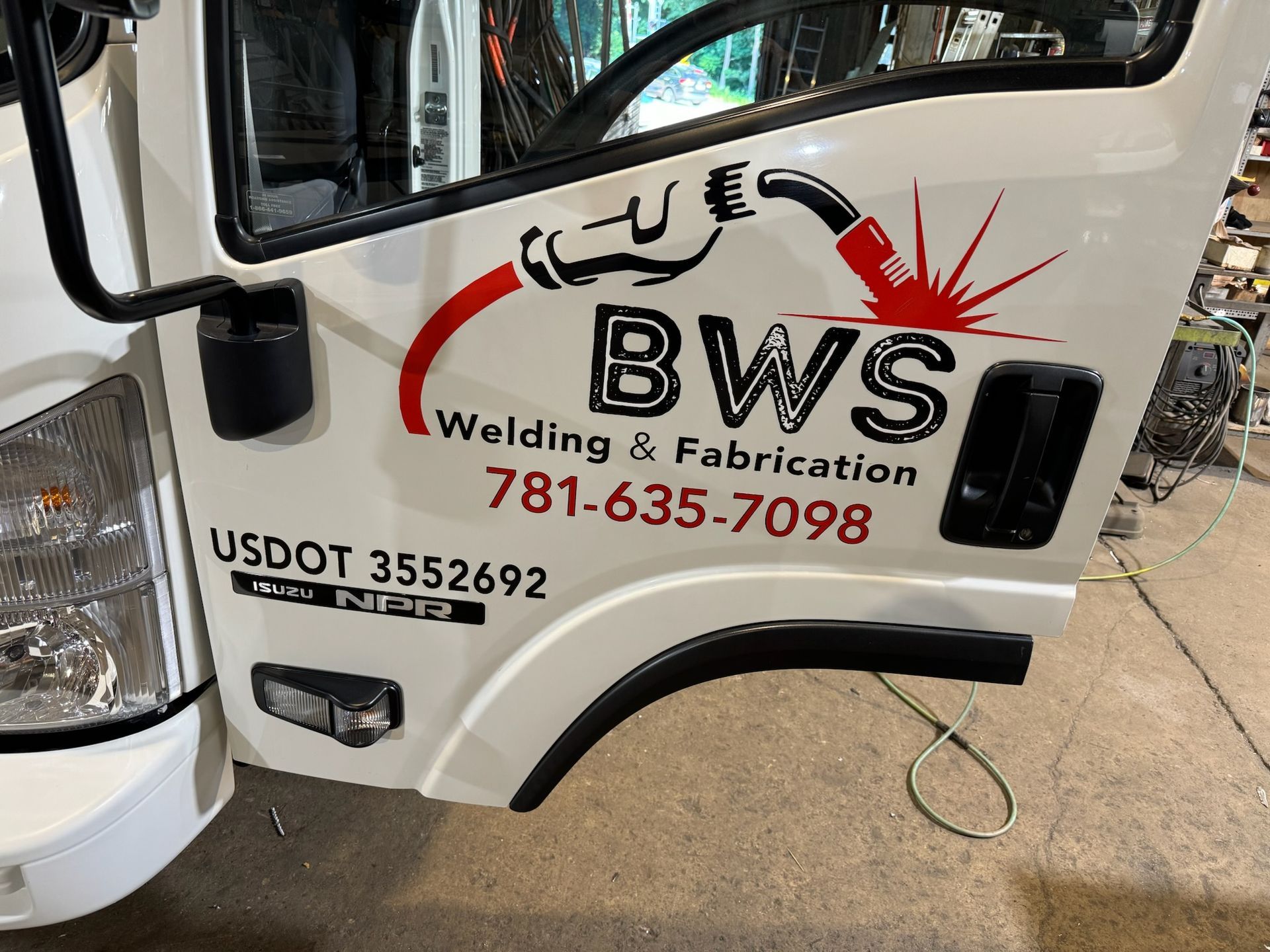 White welding truck door with BWS logo, crane graphic, and phone number on a garage floor.
