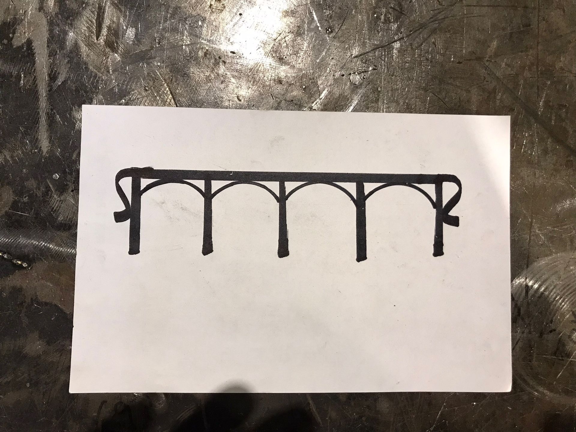 Black ink drawing of a simple arched bridge or railing on white paper.