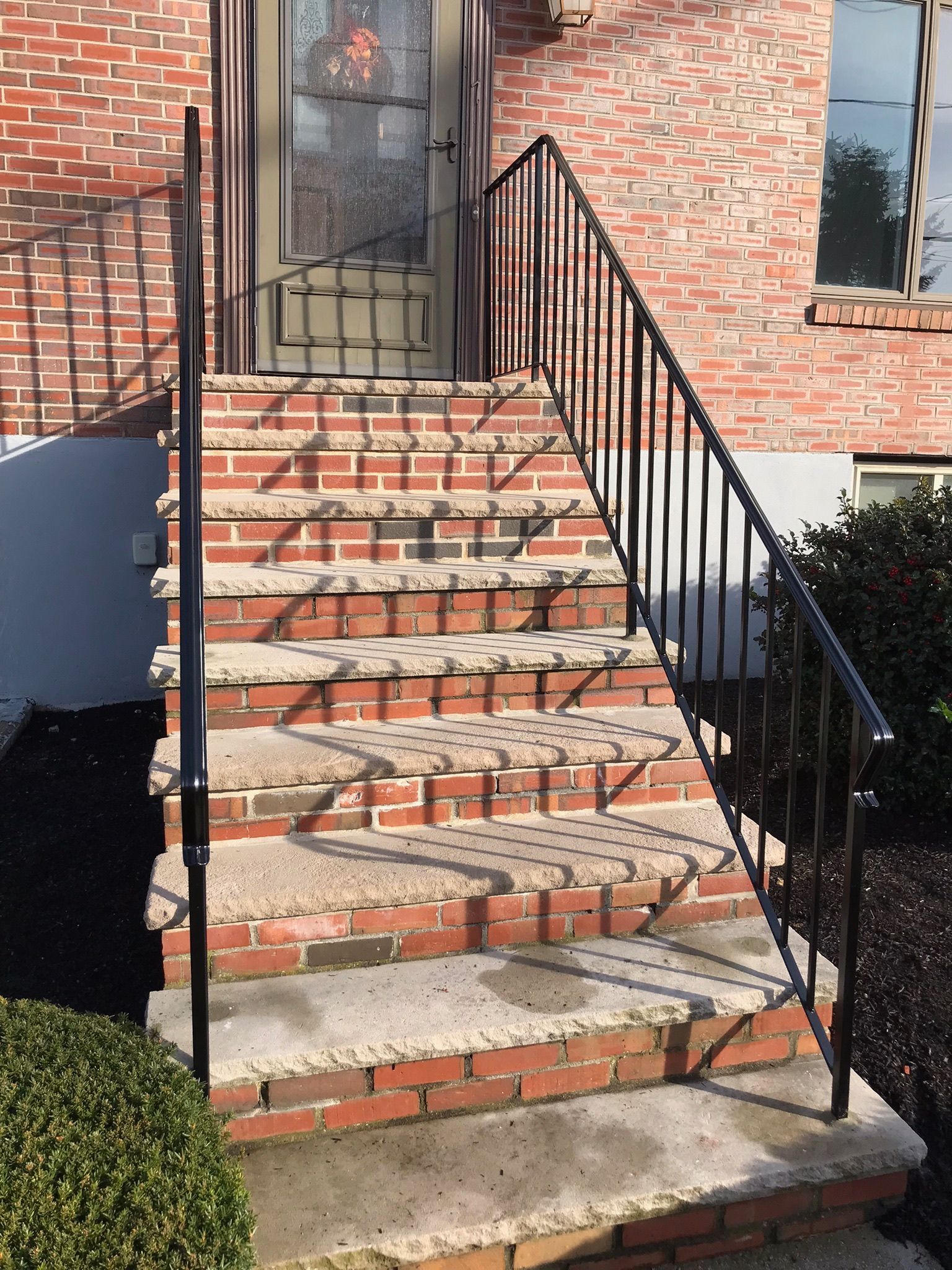 Brick front steps with black metal railings leading to a house entrance