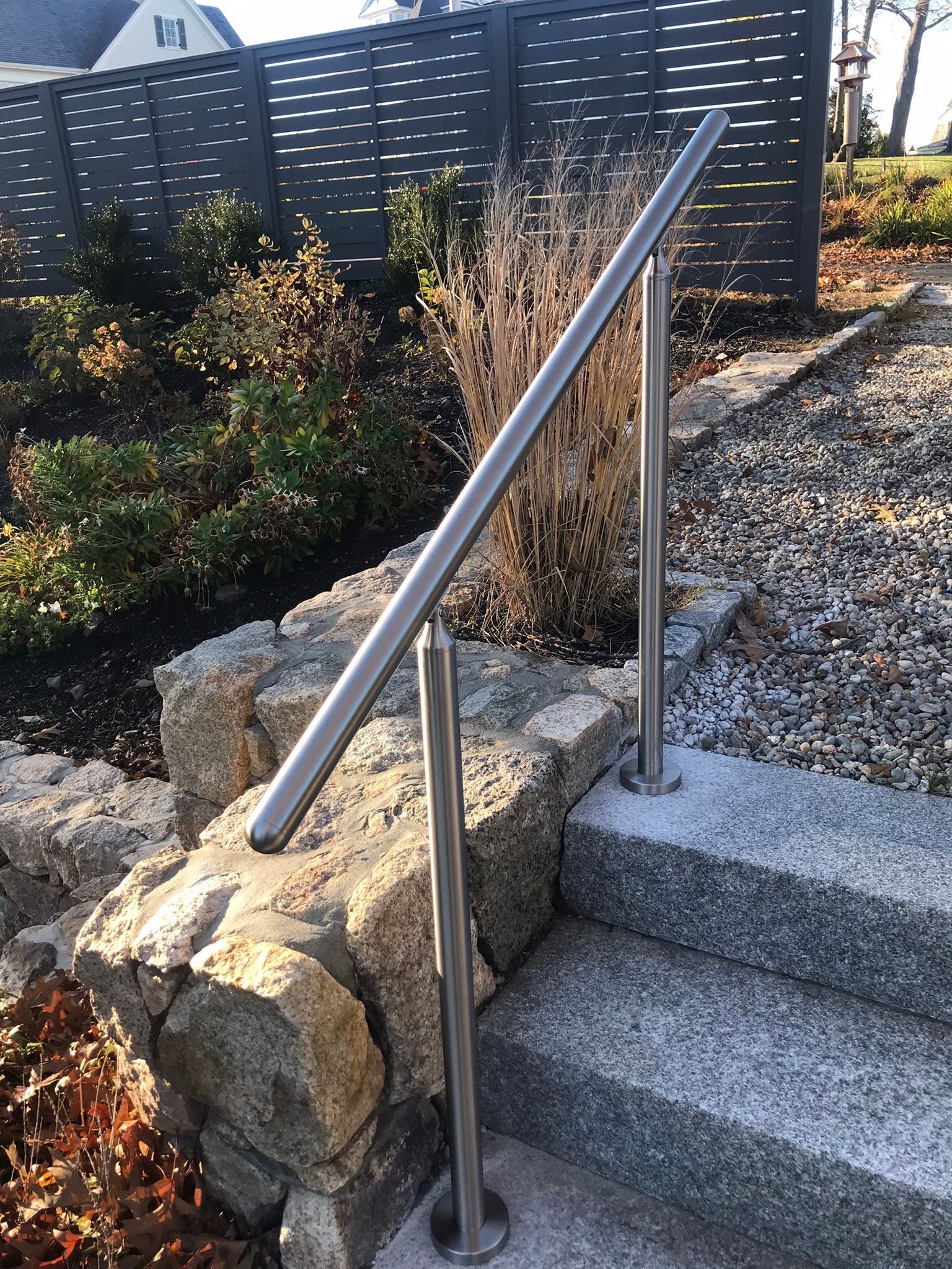 Stainless steel handrail beside outdoor stone steps with landscaped garden bed.