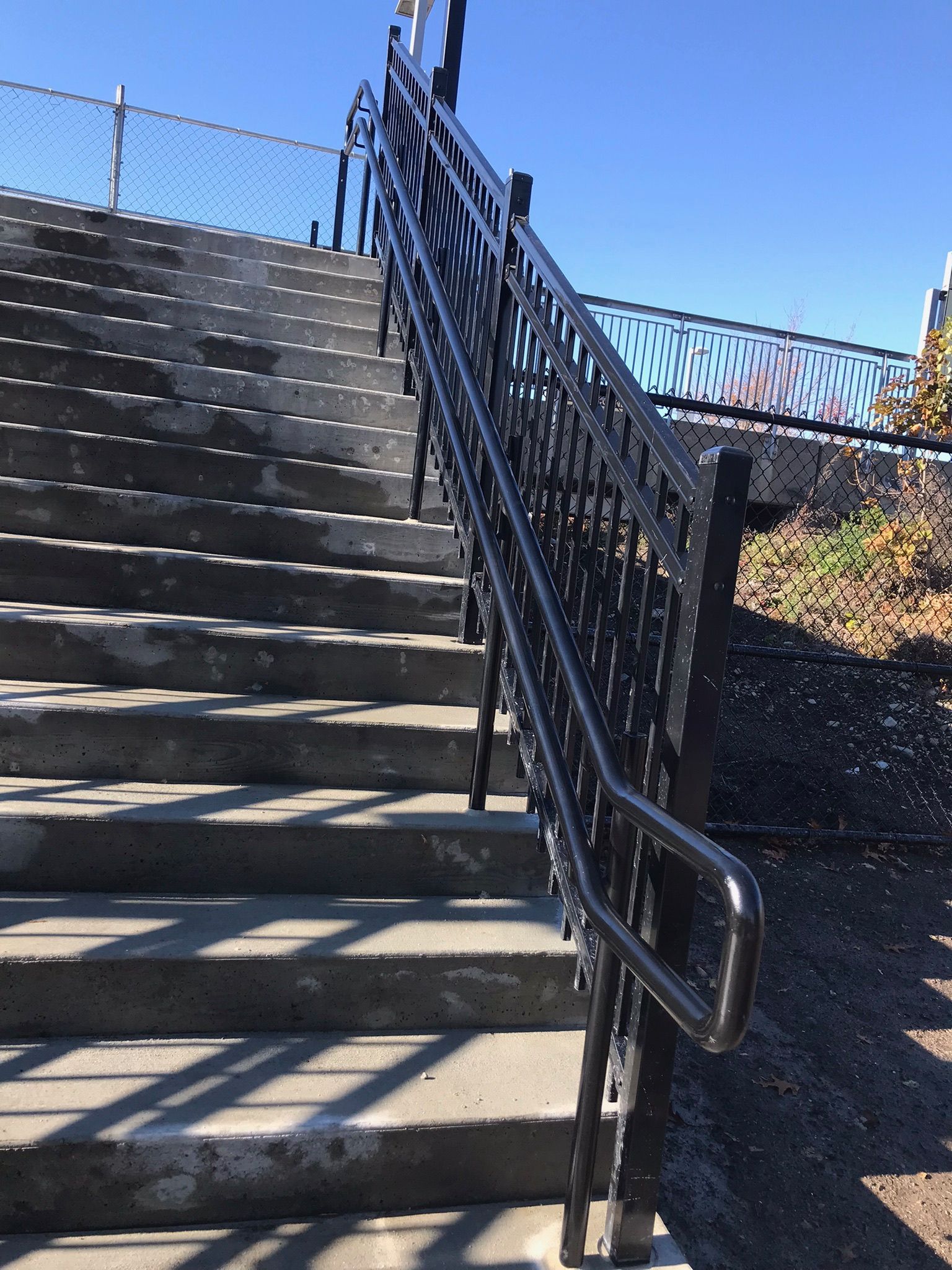 Outdoor concrete stairs with black metal railings and chain-link fencing in bright sunlight