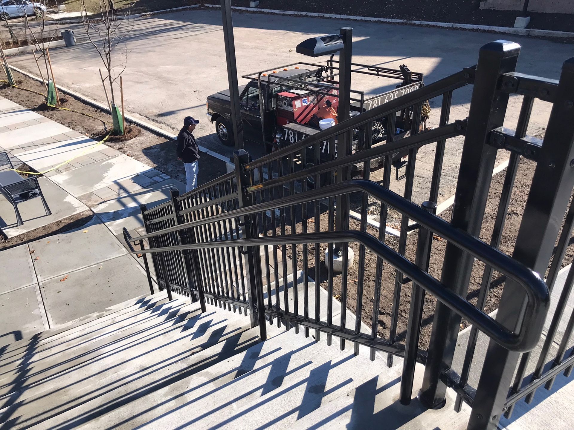Black metal handrails lining outdoor concrete steps beside a sidewalk and parking area