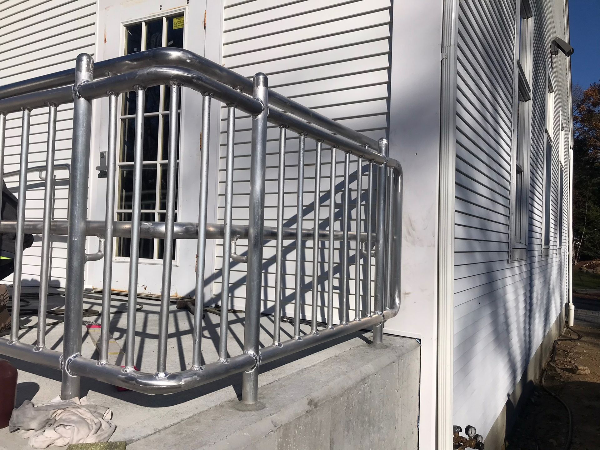 Black metal porch railing beside a house with white siding and concrete steps