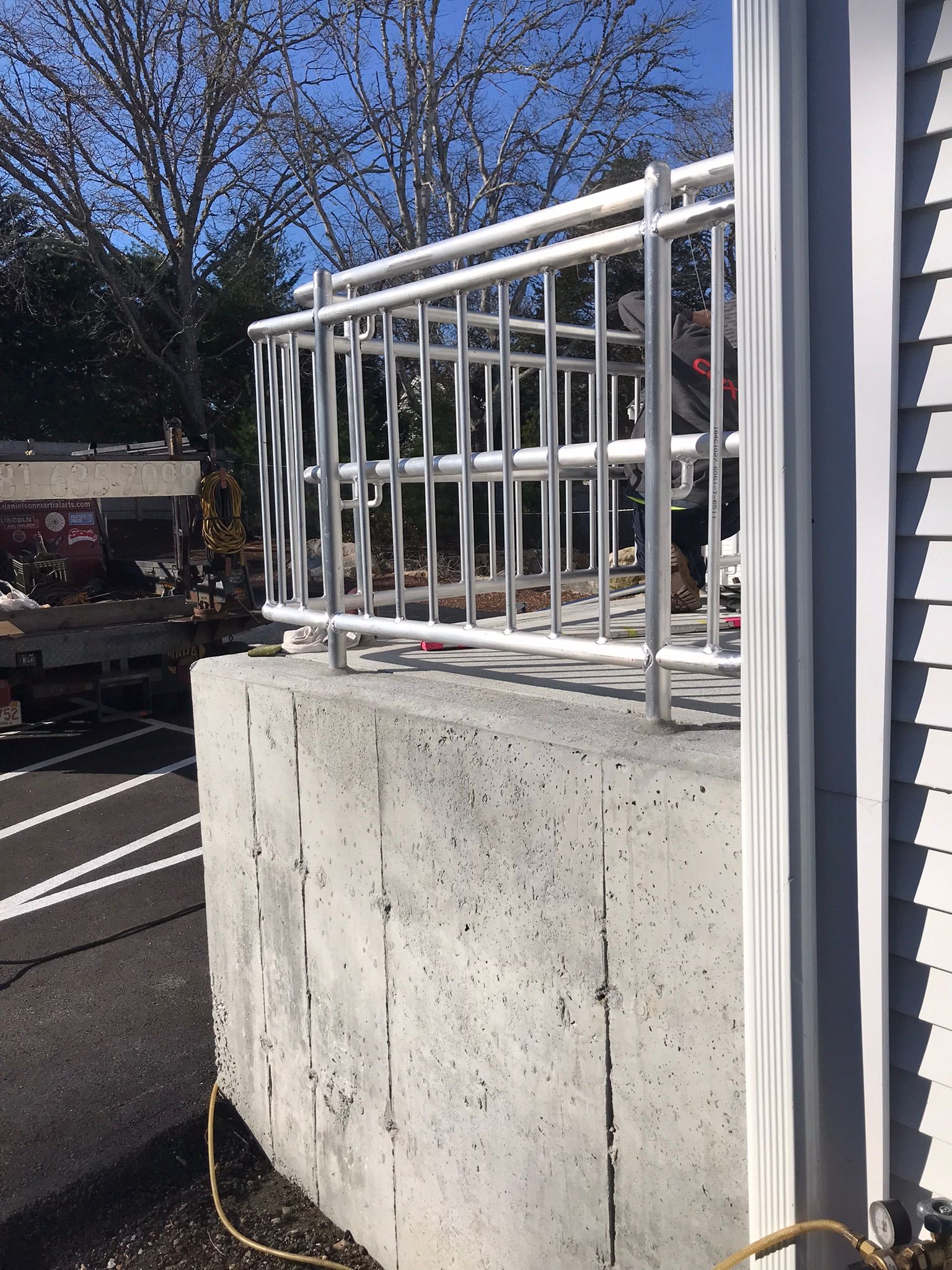 White metal railing atop a concrete wall beside a parking lot under a blue sky