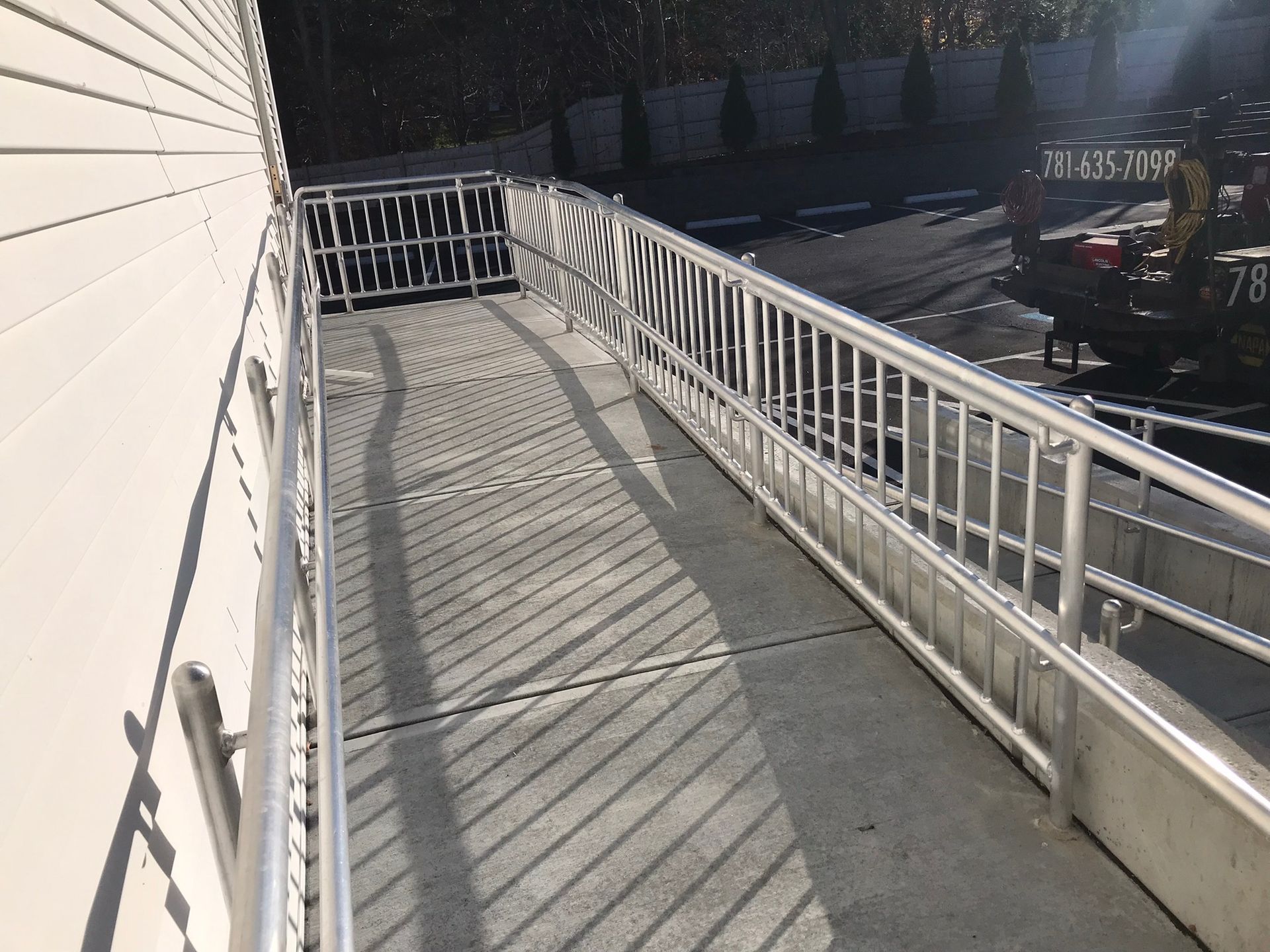 Empty concrete ramp beside a building, with white railings casting long shadows in sunlight.