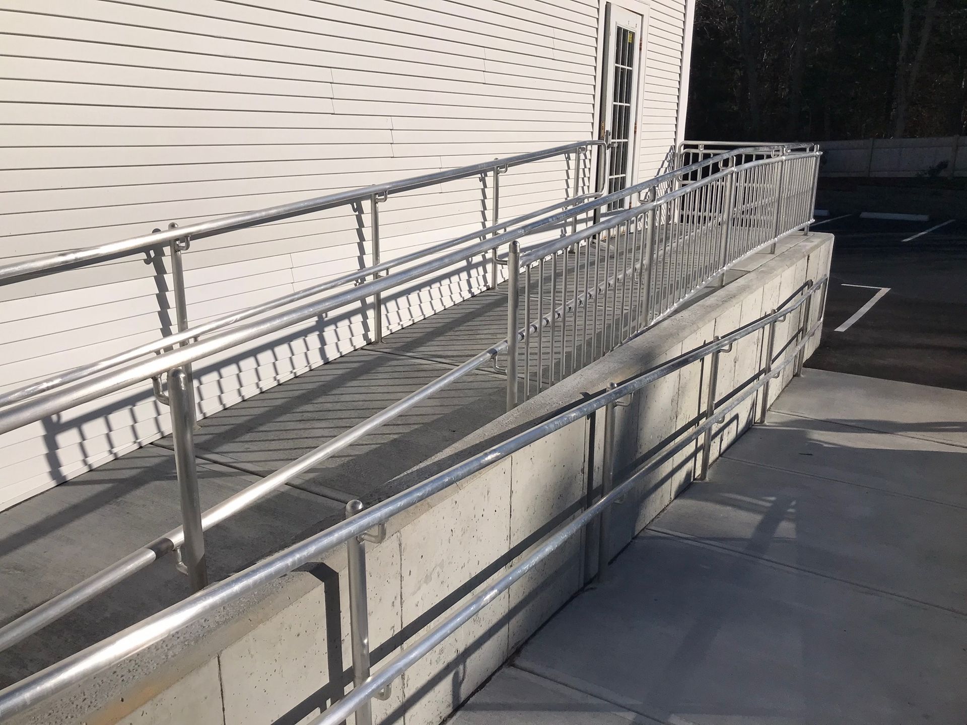 Outdoor wheelchair ramp with metal railings beside a building, lit by sunlight