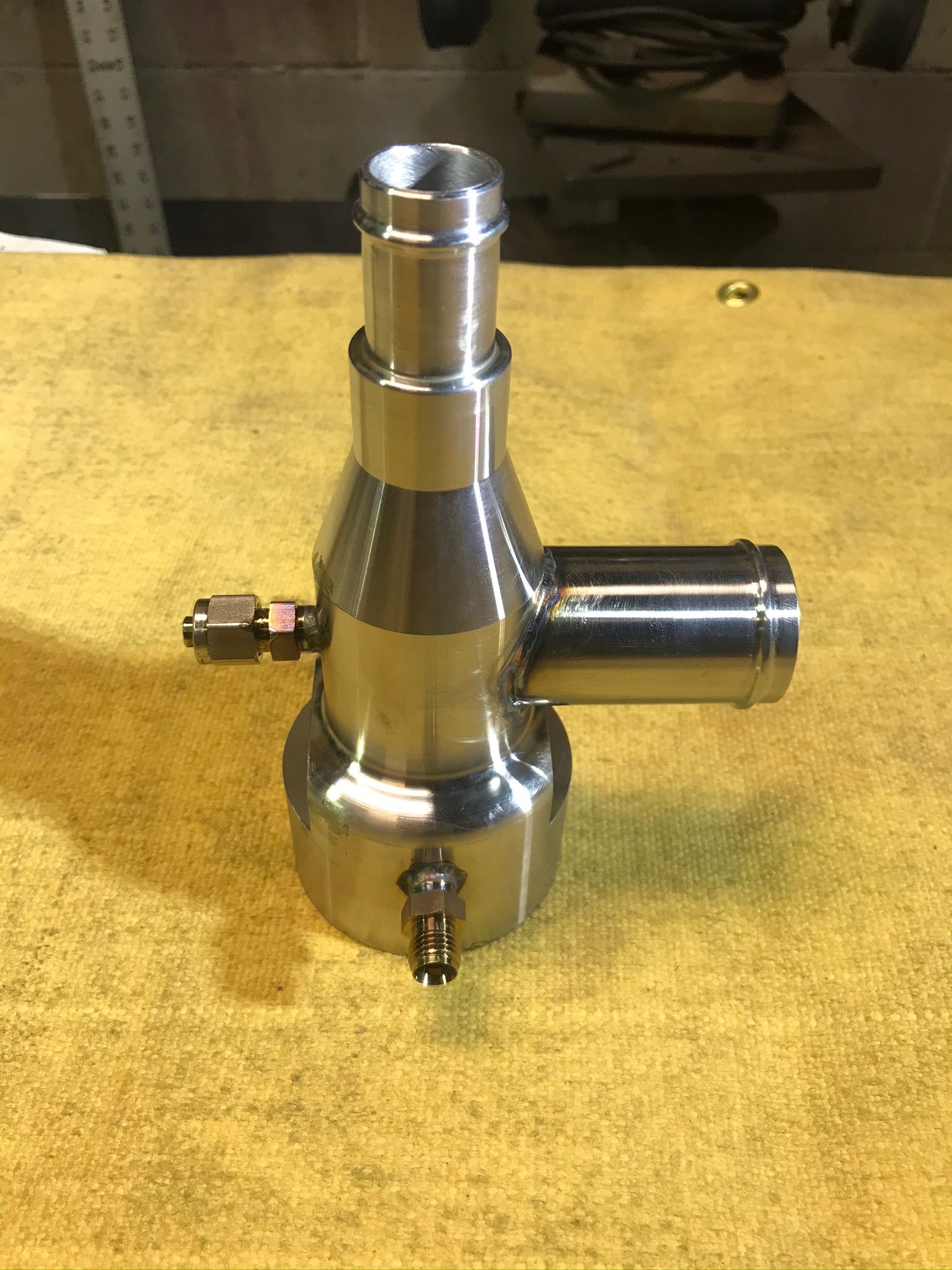 Chrome plumbing fitting with side ports on a yellow workbench