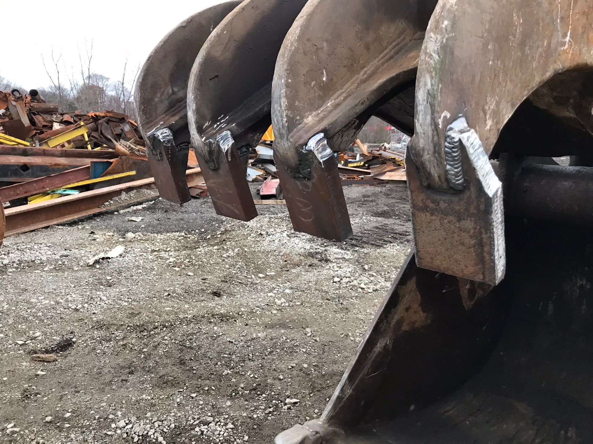 Row of large rusted metal buckets or scoops lined up on gravel at an industrial site