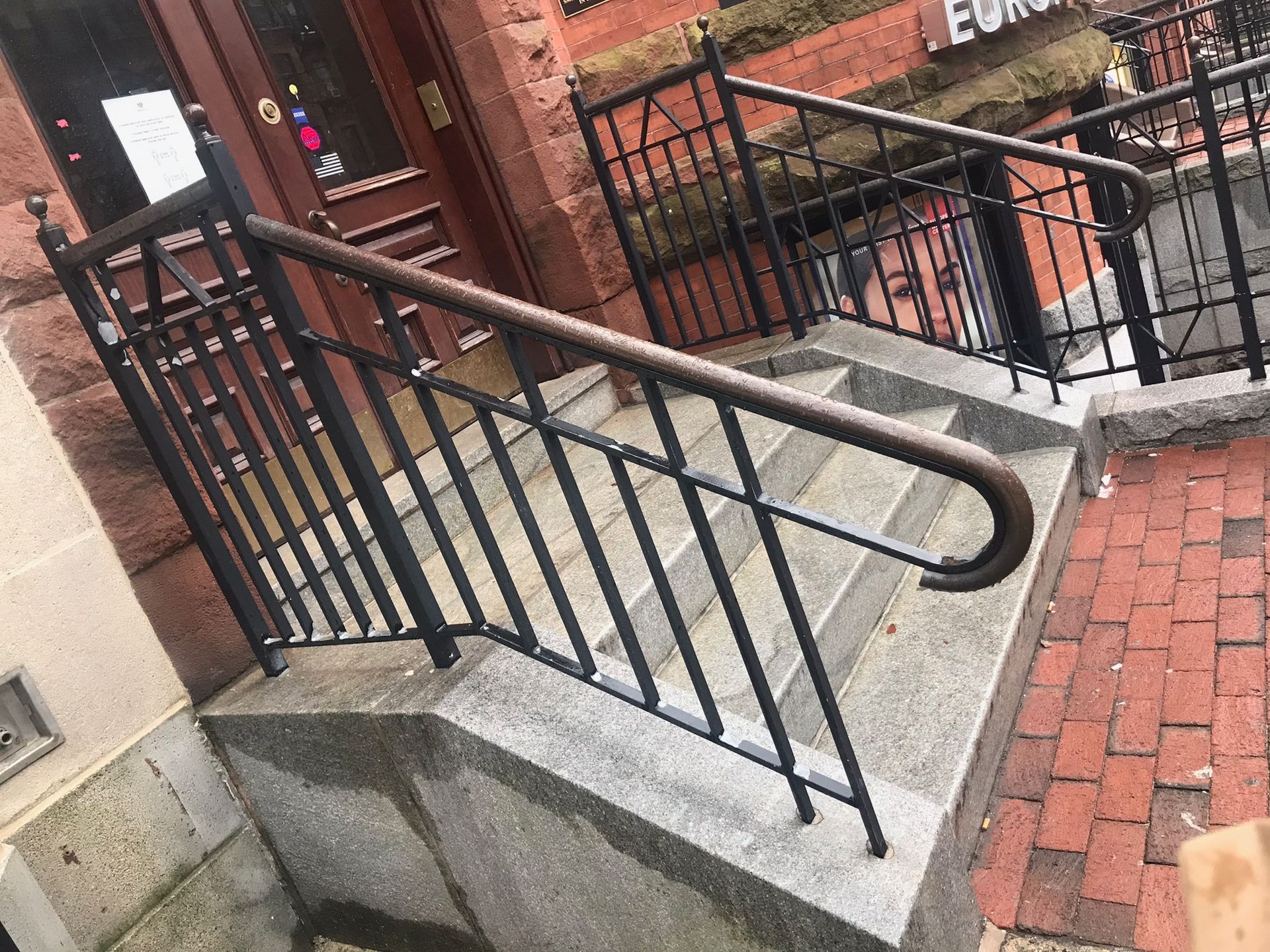 Accessible stair ramp with black railings beside a brick building and walkway