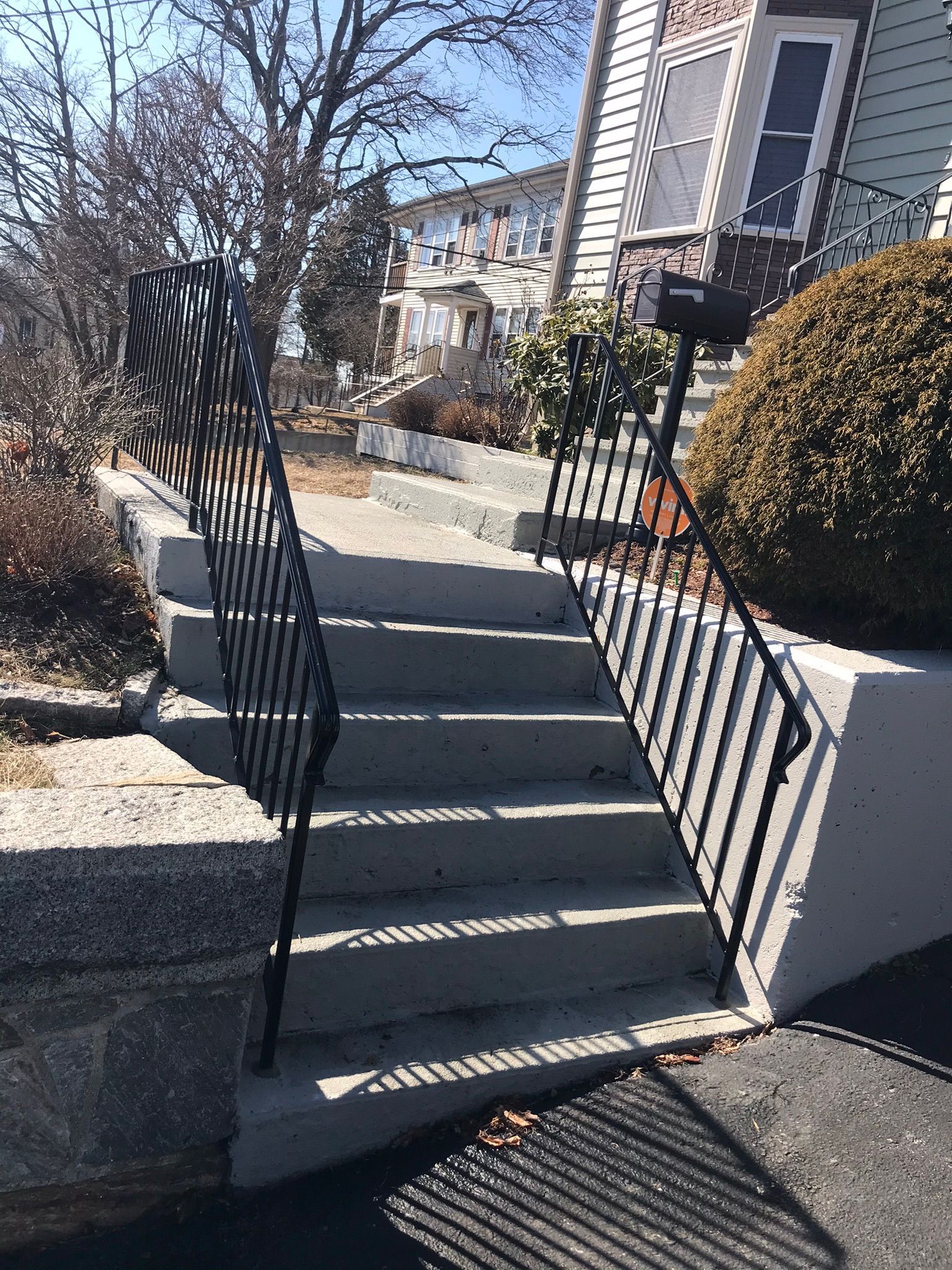 Outdoor concrete steps with black metal handrails leading up a residential walkway.