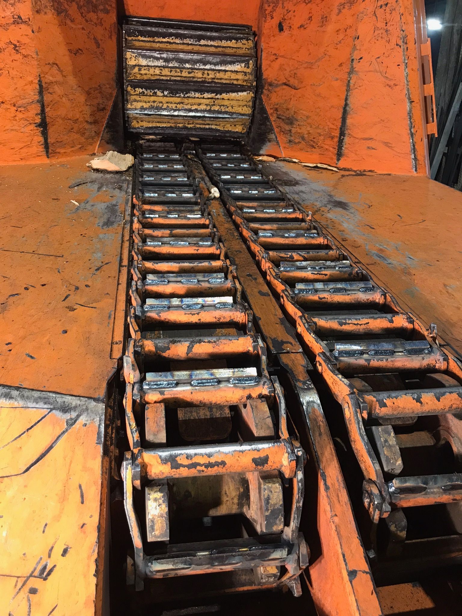 Charred metal tracks leading up a burnt orange industrial chute or ramp, covered in soot and debris