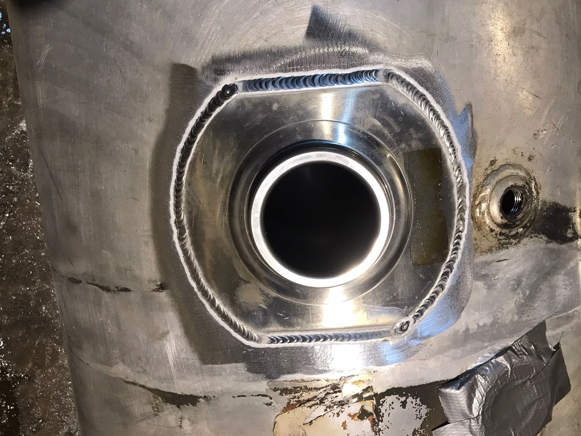 Close-up of a metal tank opening with a circular pipe fitting and welded seams.