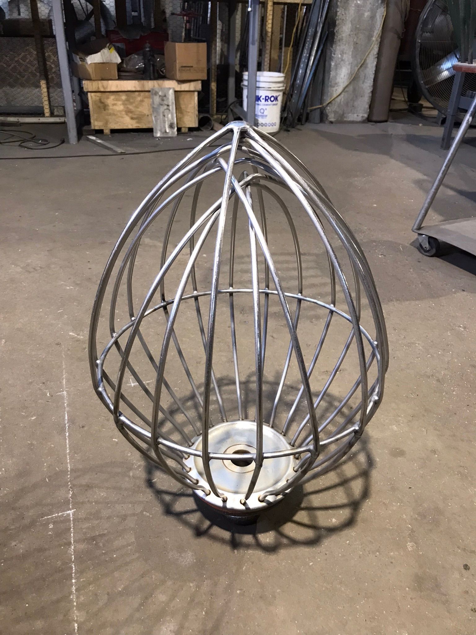 Metal wire cage hanging fixture with a white light socket, standing in a workshop floor area.