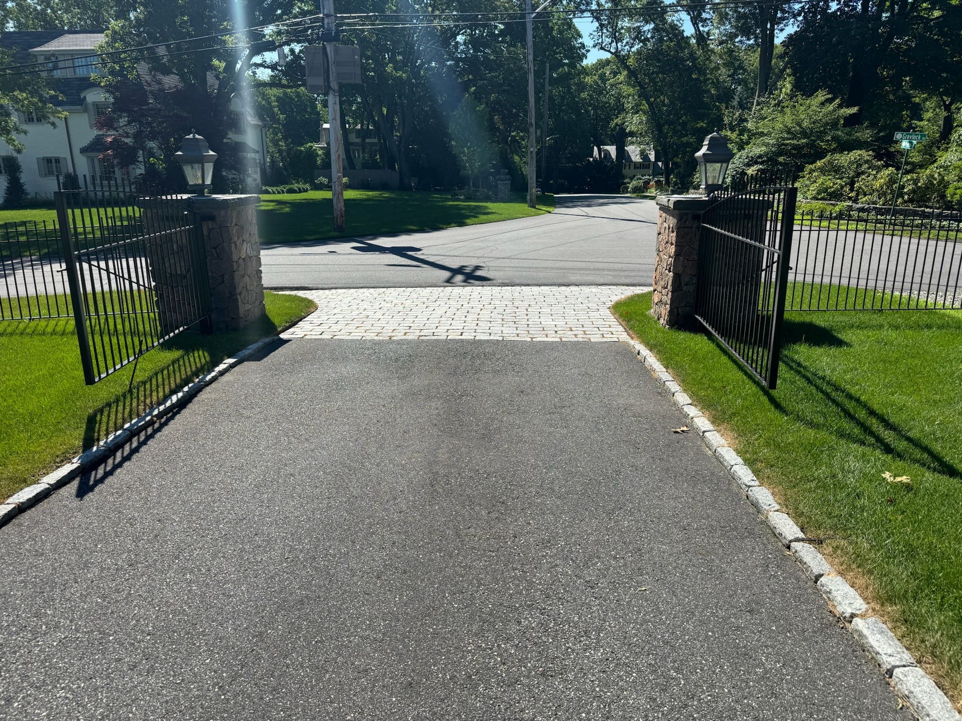 Open stone gate to a tree-lined driveway in bright sunlight